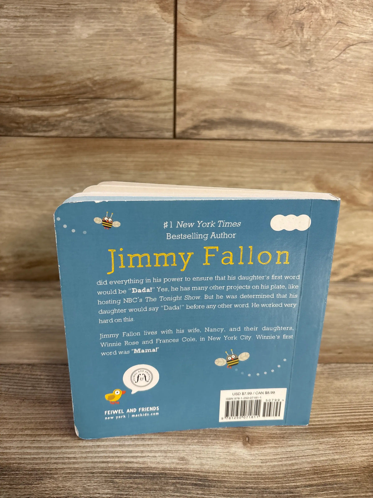 Back cover of Your Baby’s First Word Will Be Dada board book with Jimmy Fallon text and bee illustrations on a wood surface