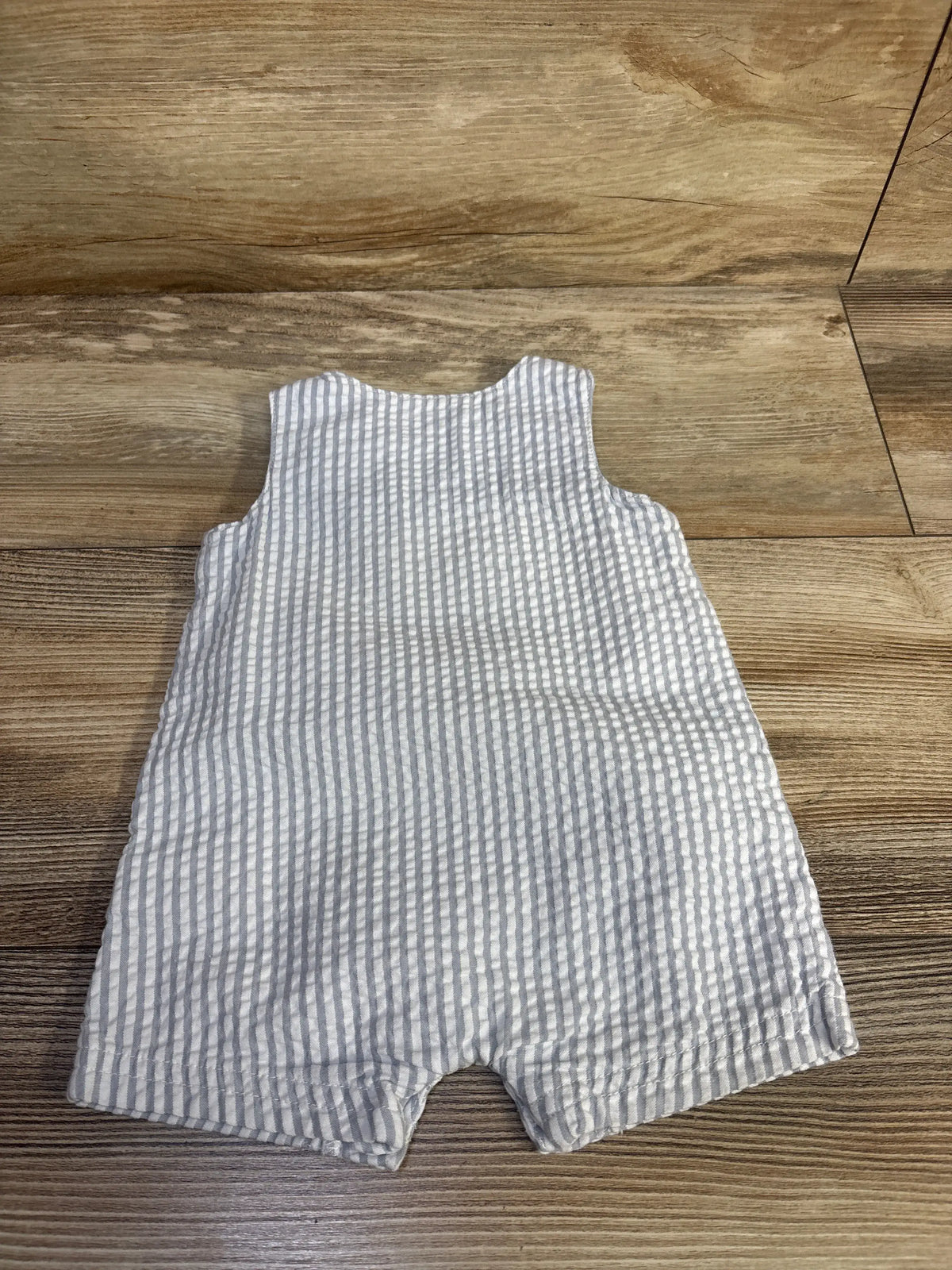 Little Me white and grey seersucker baby romper laid flat on a wooden surface