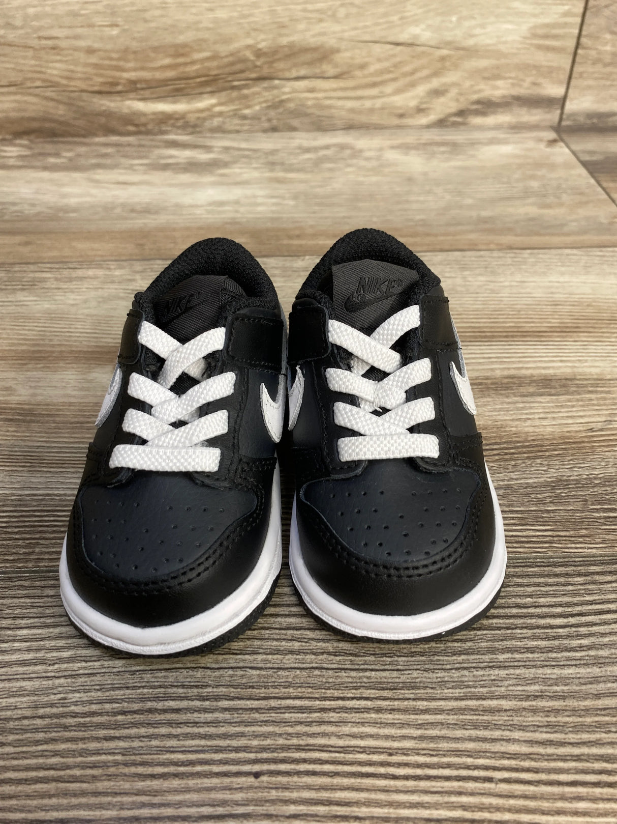 Black and white Nike toddler sneakers on a wood floor