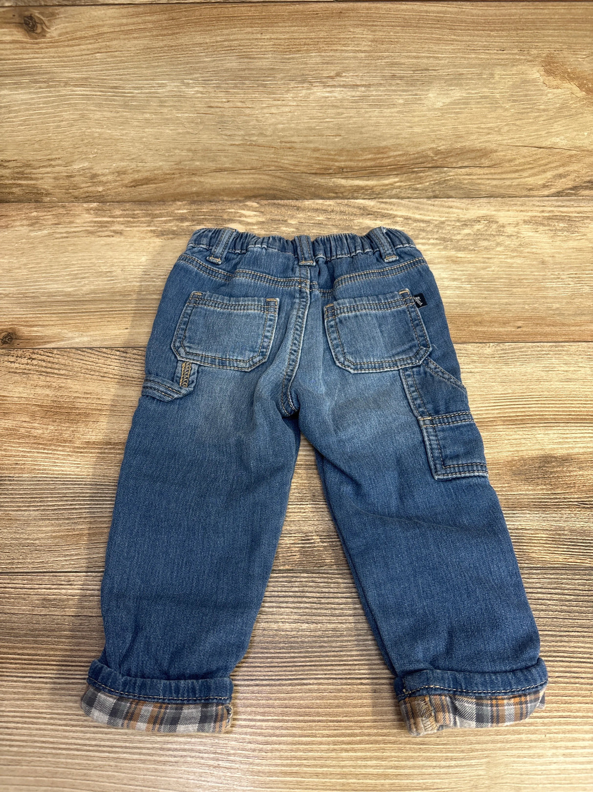 Back view of toddler boys' denim jeans with plaid cuff detail on wooden background