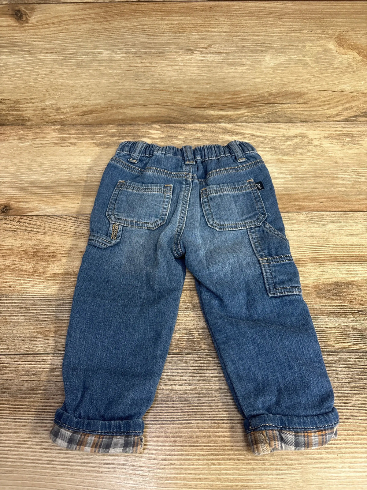 Back view of toddler boys' denim jeans with plaid cuff detail on wooden background