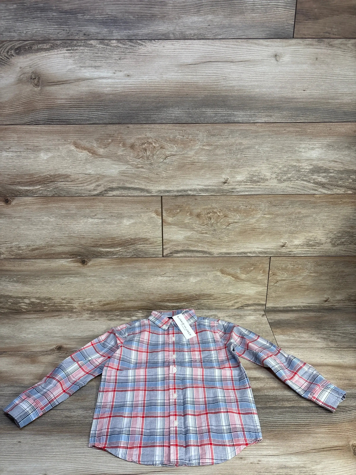 Flat lay of boys’ red, white and blue plaid button-down shirt showing front buttons, collar and long sleeves on wood floor background