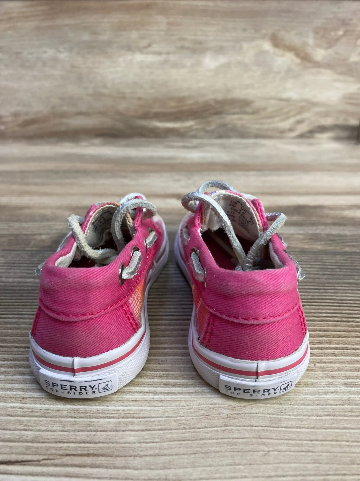 Rear view of Sperry Top-Sider toddler pink plaid canvas boat shoes showcasing heel logo and white rubber sole on wood background