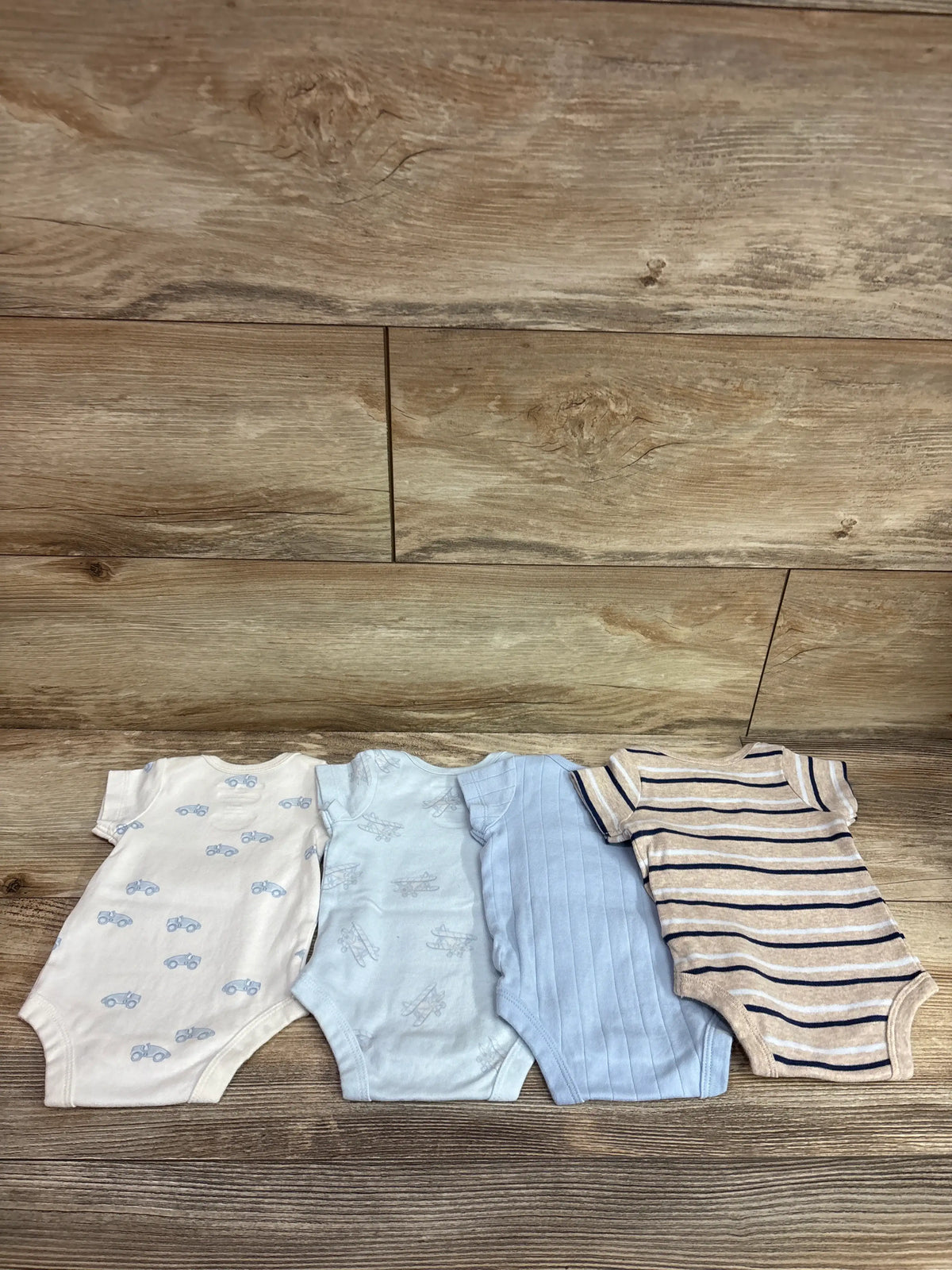 Member's Mark 4pk organic bodysuits for newborns in blue and white patterns on wood background