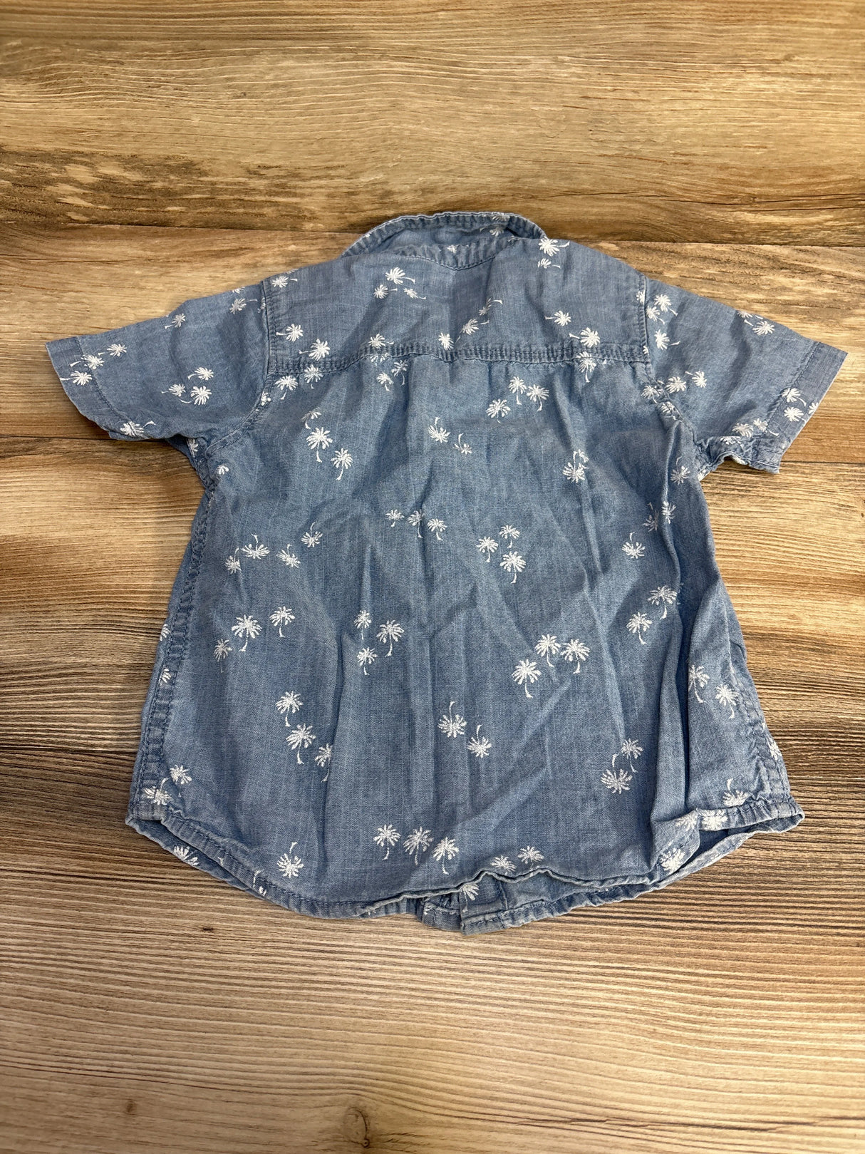 Blue short sleeve denim shirt with white palm tree print on wood background