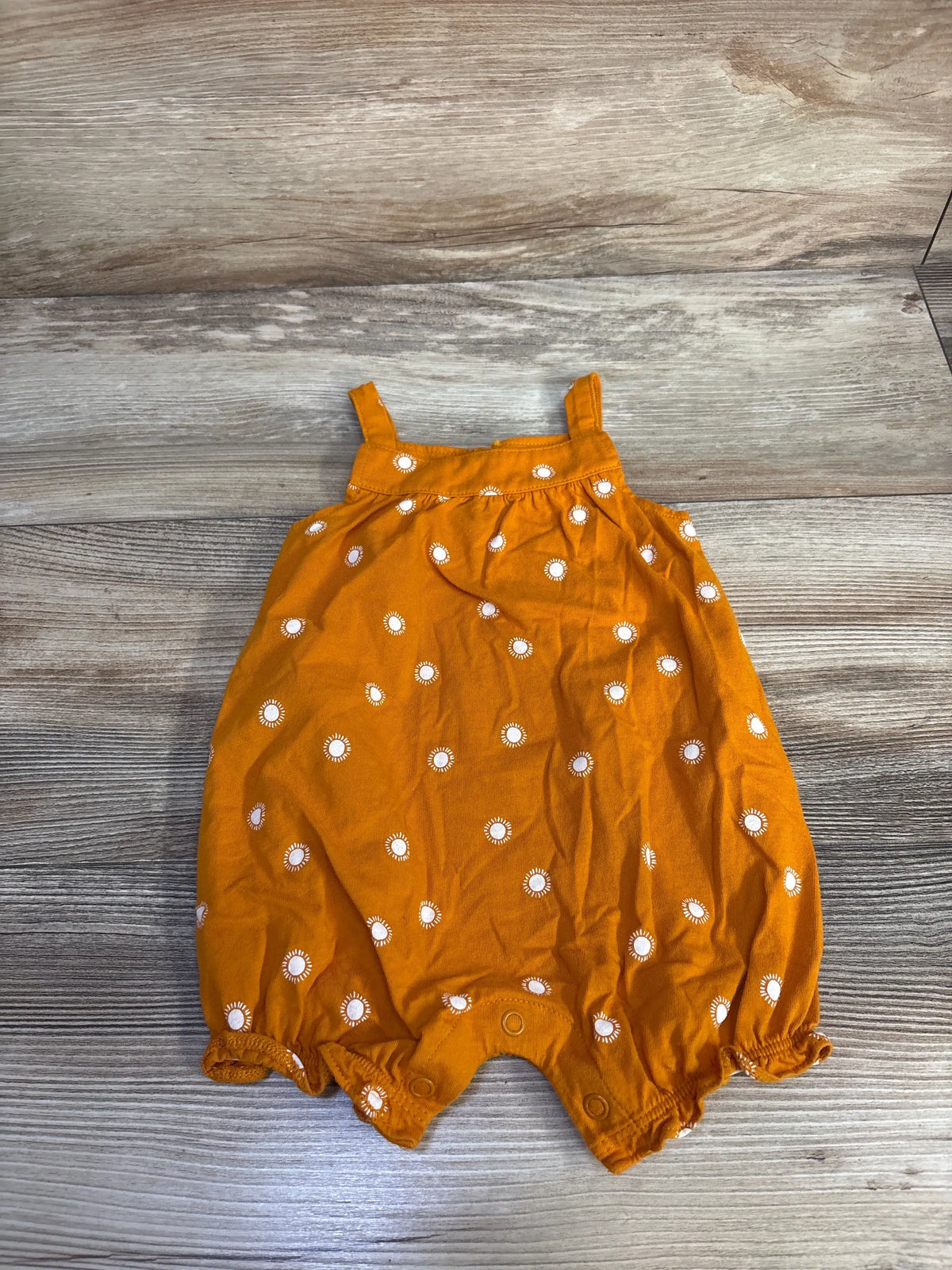 Front view of Carter’s orange shortie romper showcasing white sunburst print and snap closures with wood-look background