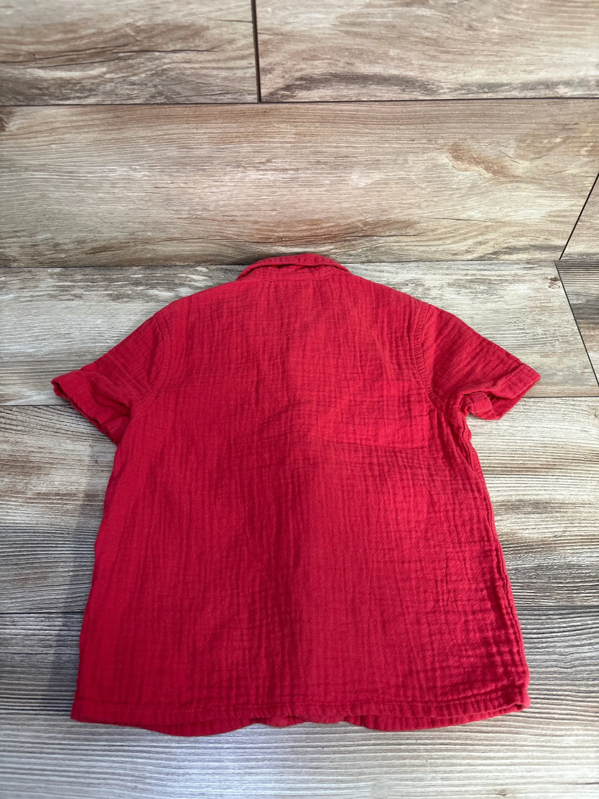 Back view of Jumping Beans red gauze button-up shirt in size 2T showcasing short sleeves and textured cotton fabric on a wood surface
