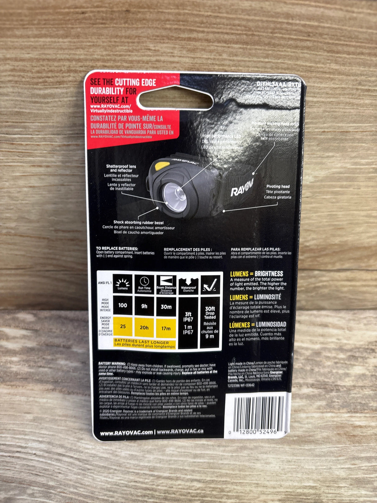 Rear view of Rayovac Virtually Indestructible LED headlamp packaging showing specifications, feature callouts, and barcode on a wood surface