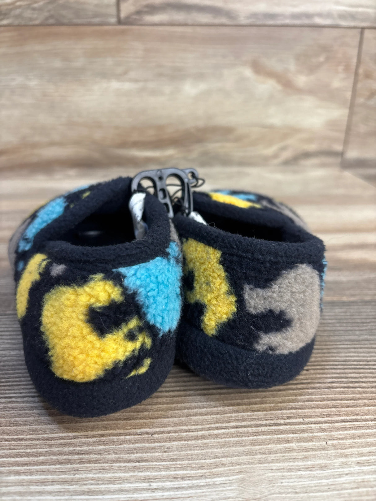 Plush fleece baby booties with yellow, blue, and beige animal print on wood background