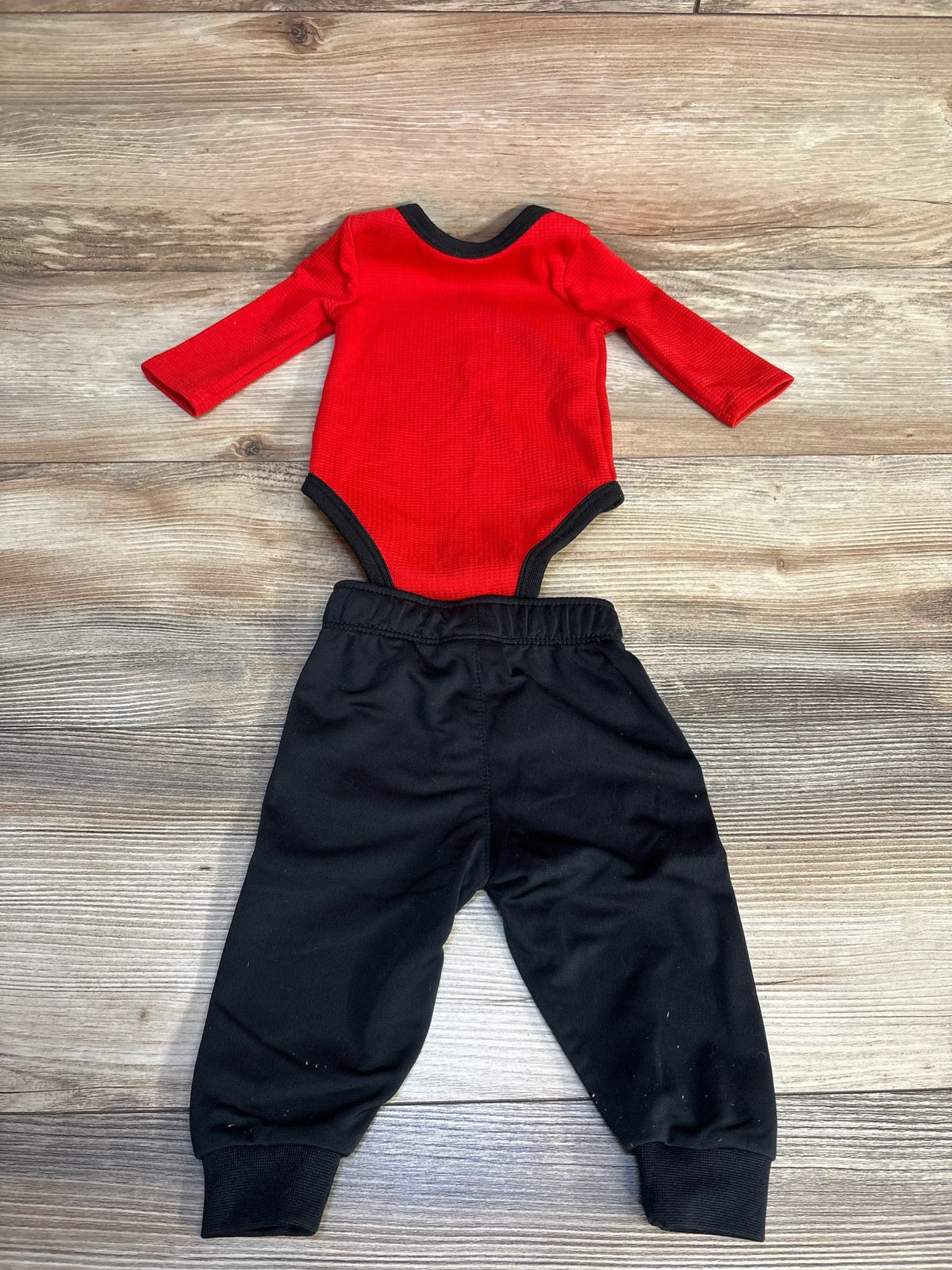 Red long-sleeve baby onesie with black trim paired with black jogger pants, laid flat on wood floor