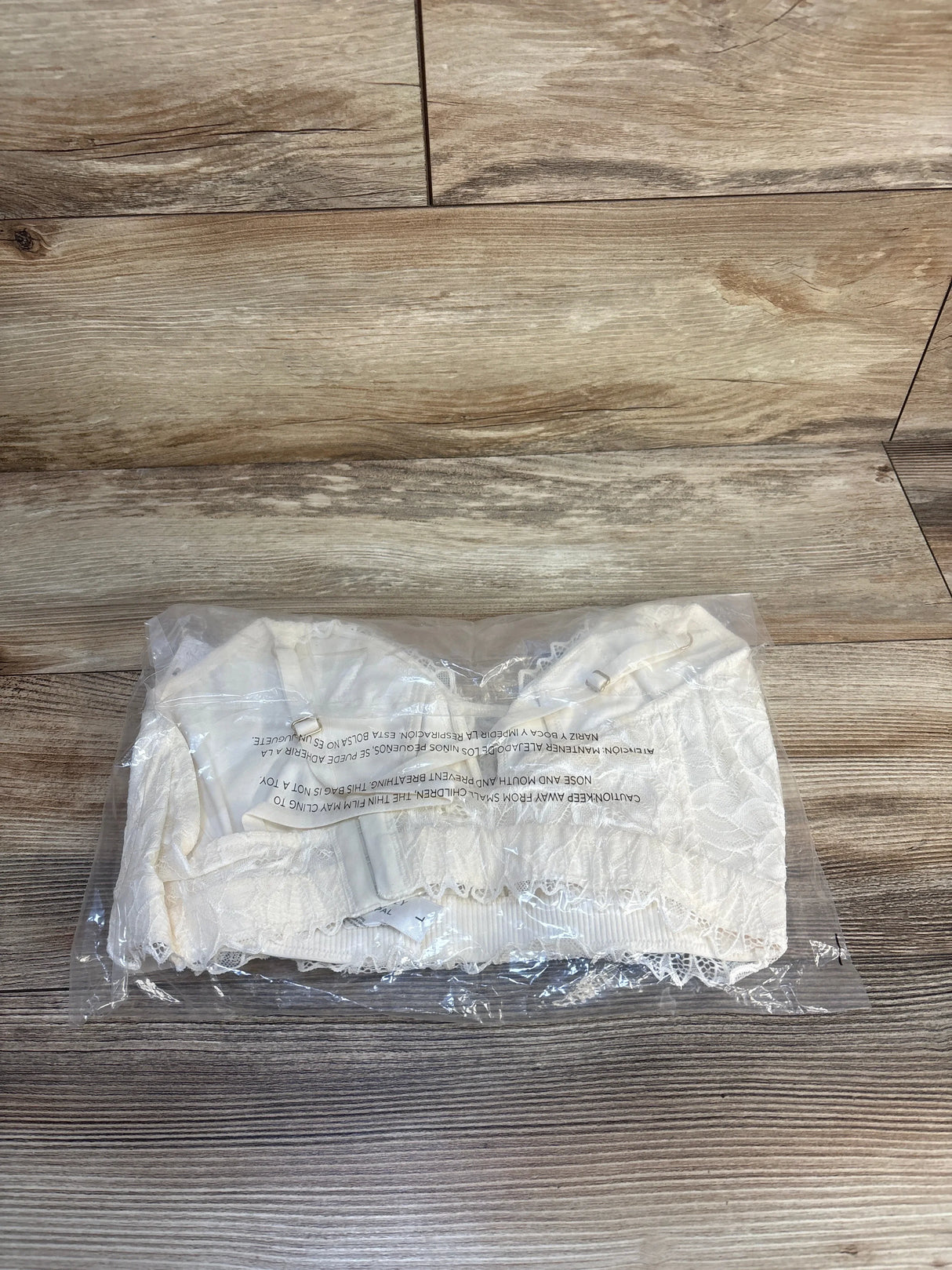 White lace bandeau top sealed in plastic packaging on wood floor