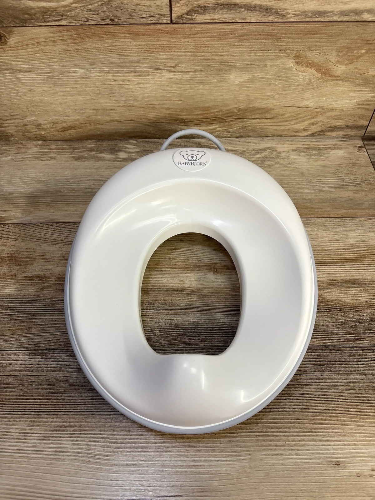 Top view of Baby Bjorn Toilet Trainer Seat showcasing its handle and splashguard on a wood surface