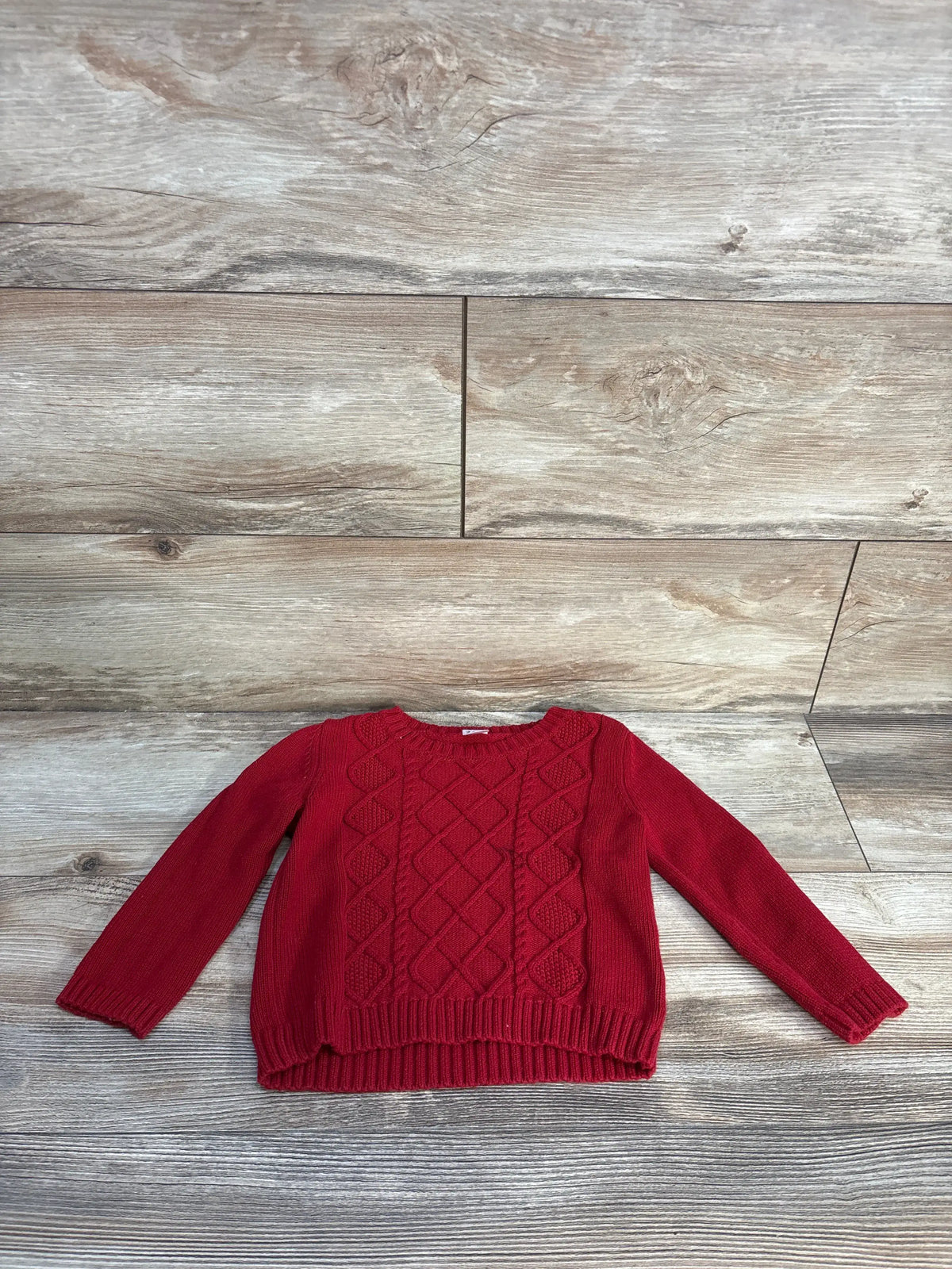 Front view of Carter’s red cable knit sweater, size 24 months, showcasing cable-knit texture and ribbed trim on a wood-look floor