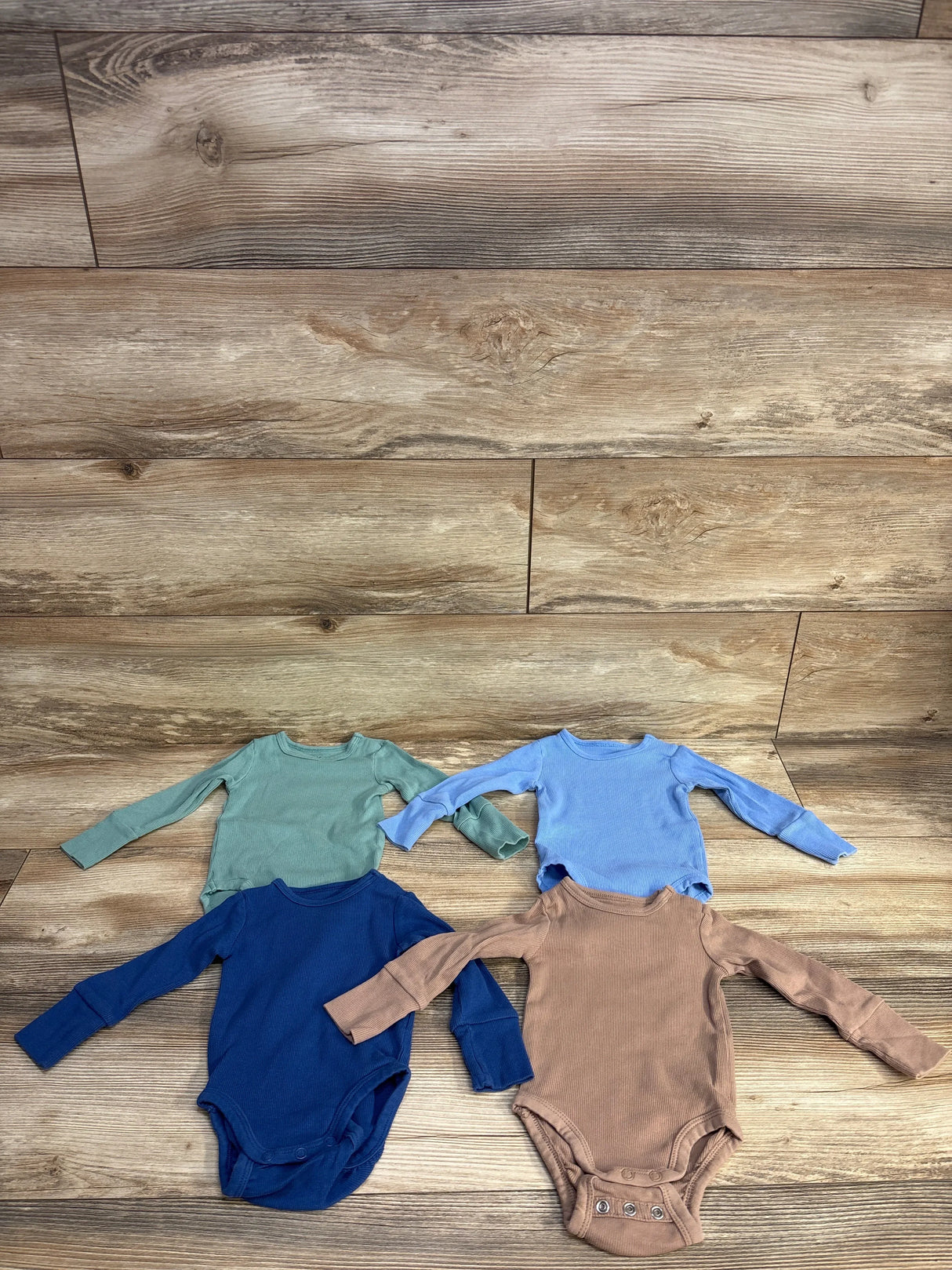 Set of four long sleeve baby bodysuits in green, blue, navy, and brown on wood floor