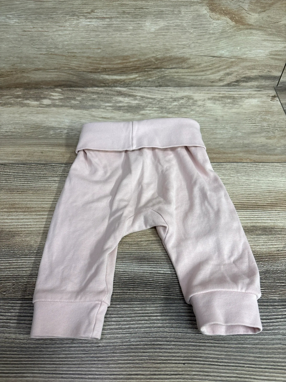 Flat lay of H&M Foldover-Waist Pants sz 3m in soft pink with wide foldover waistband and ribbed cuffs on wood plank floor