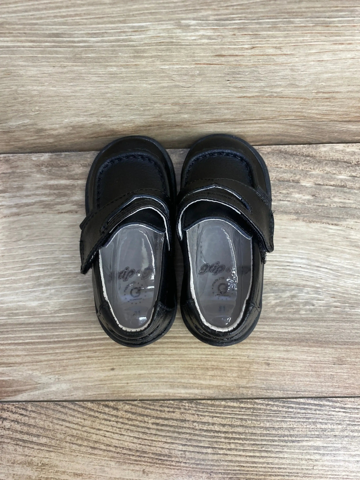 Top-down view of black Pediped Charlie toddler loafers showcasing hook-and-loop strap with wood plank background