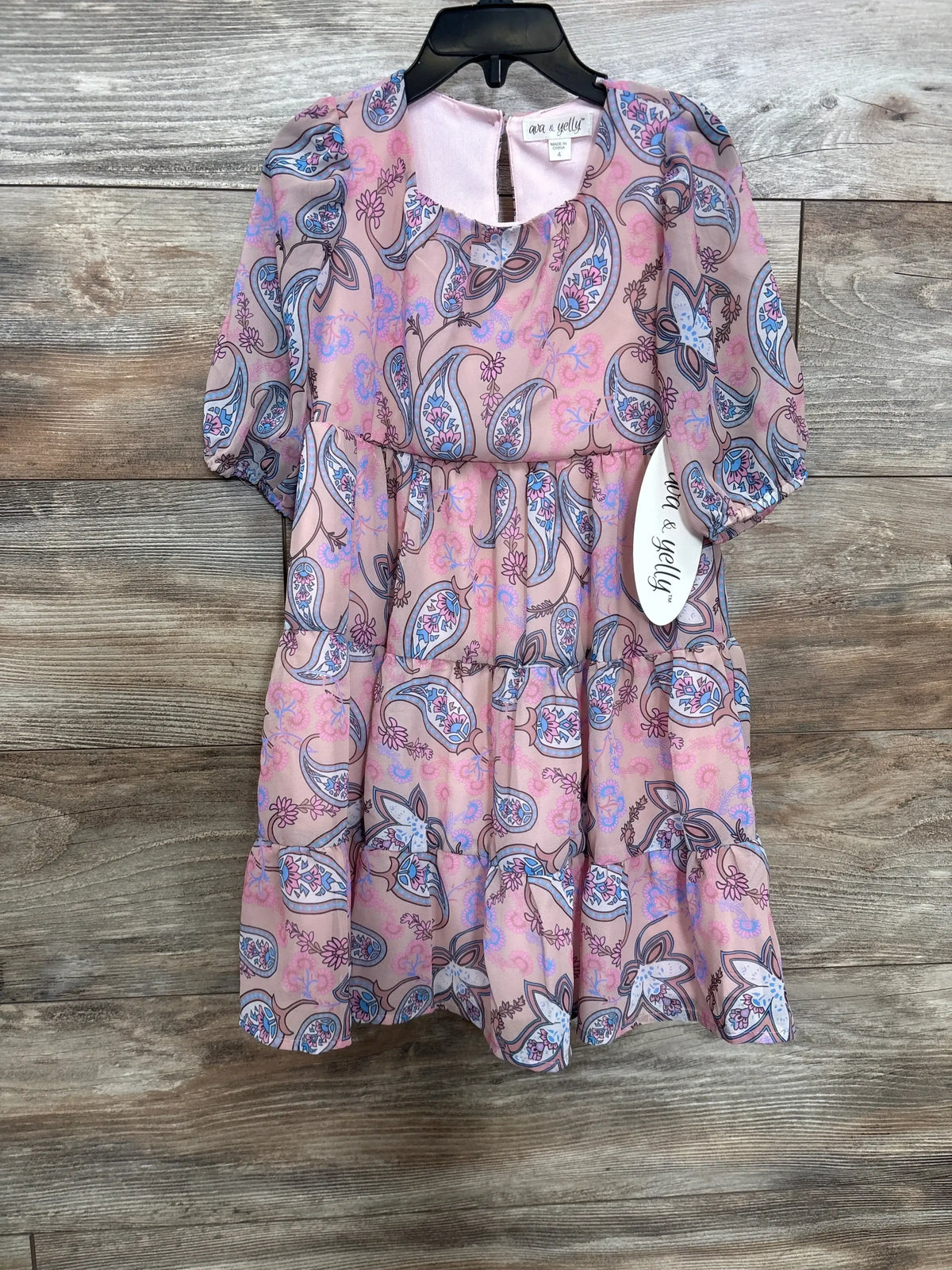 Front view of dusty rose paisley tiered girls' dress with puff sleeves, gathered tiers and visible 4T tag on wood background