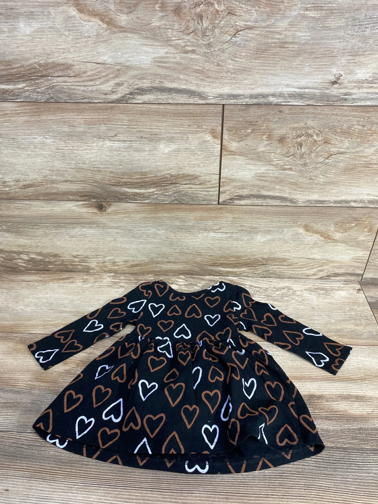 Flat lay of Cat & Jack long-sleeve toddler dress showing brown and white heart print on black fabric on wood floor