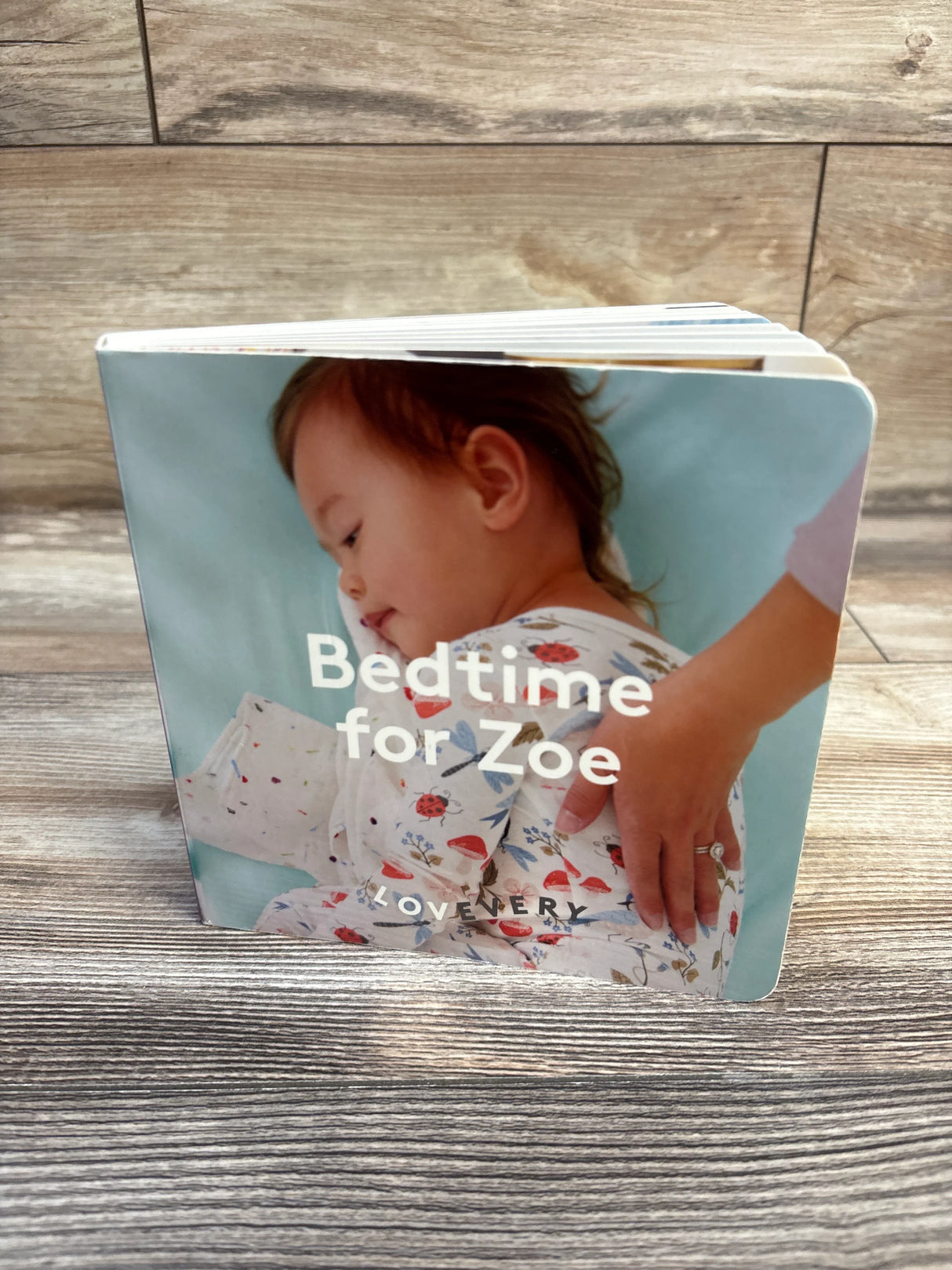 Front view of Lovevery 'Bedtime for Zoe' board book showcasing personalized cover with child in floral pajamas on wood floor