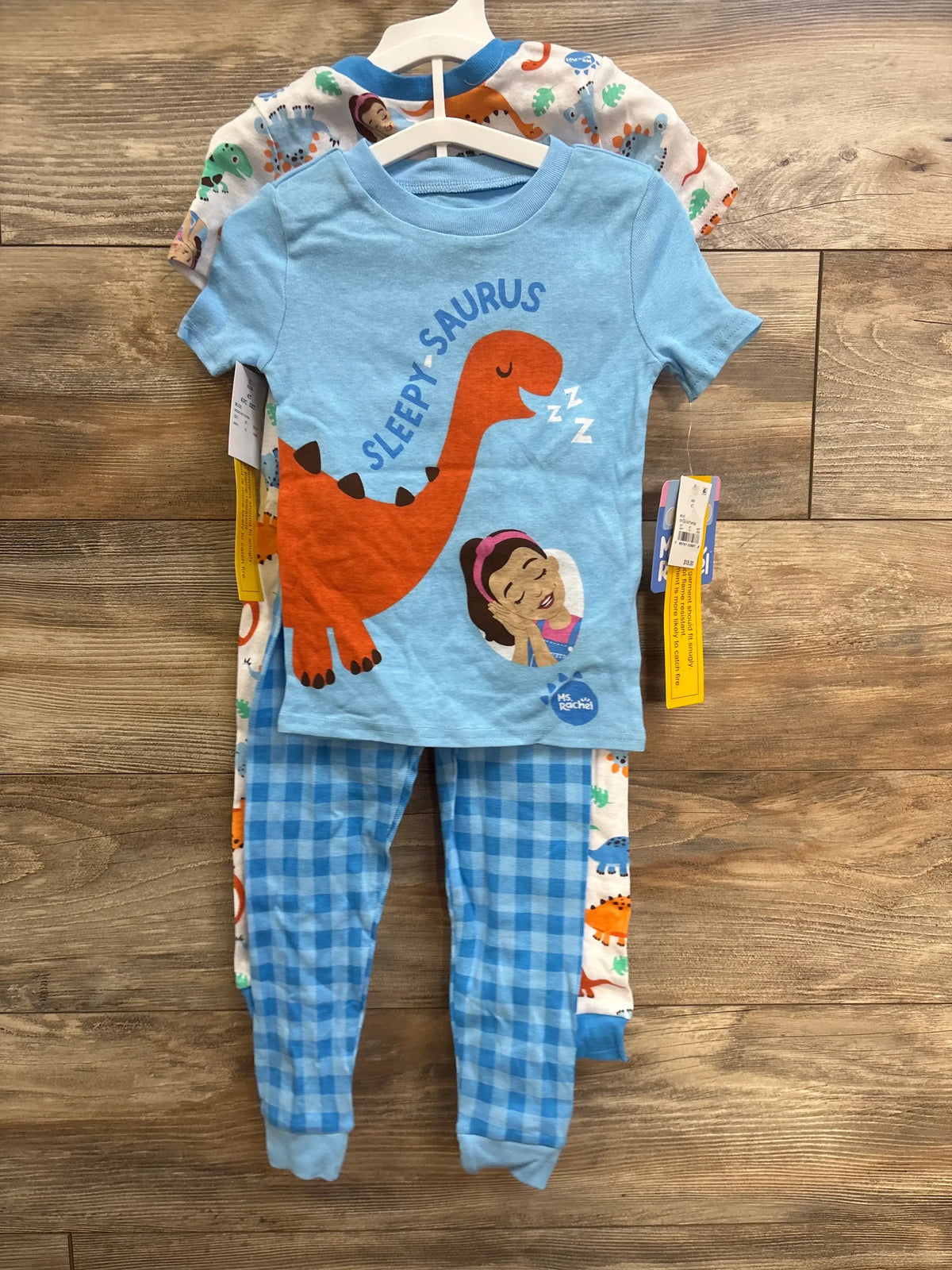 Front view of NEW Ms Rachel 4T four piece blue cotton pajama set with dinosaur and checkered prints on a wood floor
