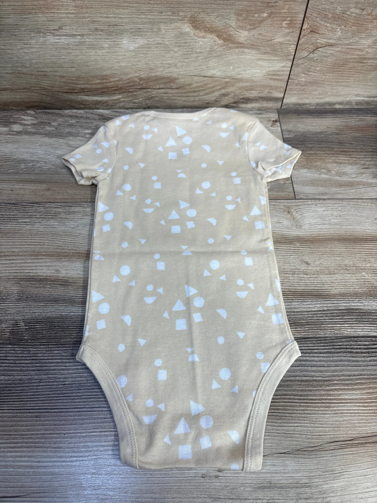 Front view of pale yellow Okie Dokie toddler bodysuit showcasing a white geometric pattern on a wood floor