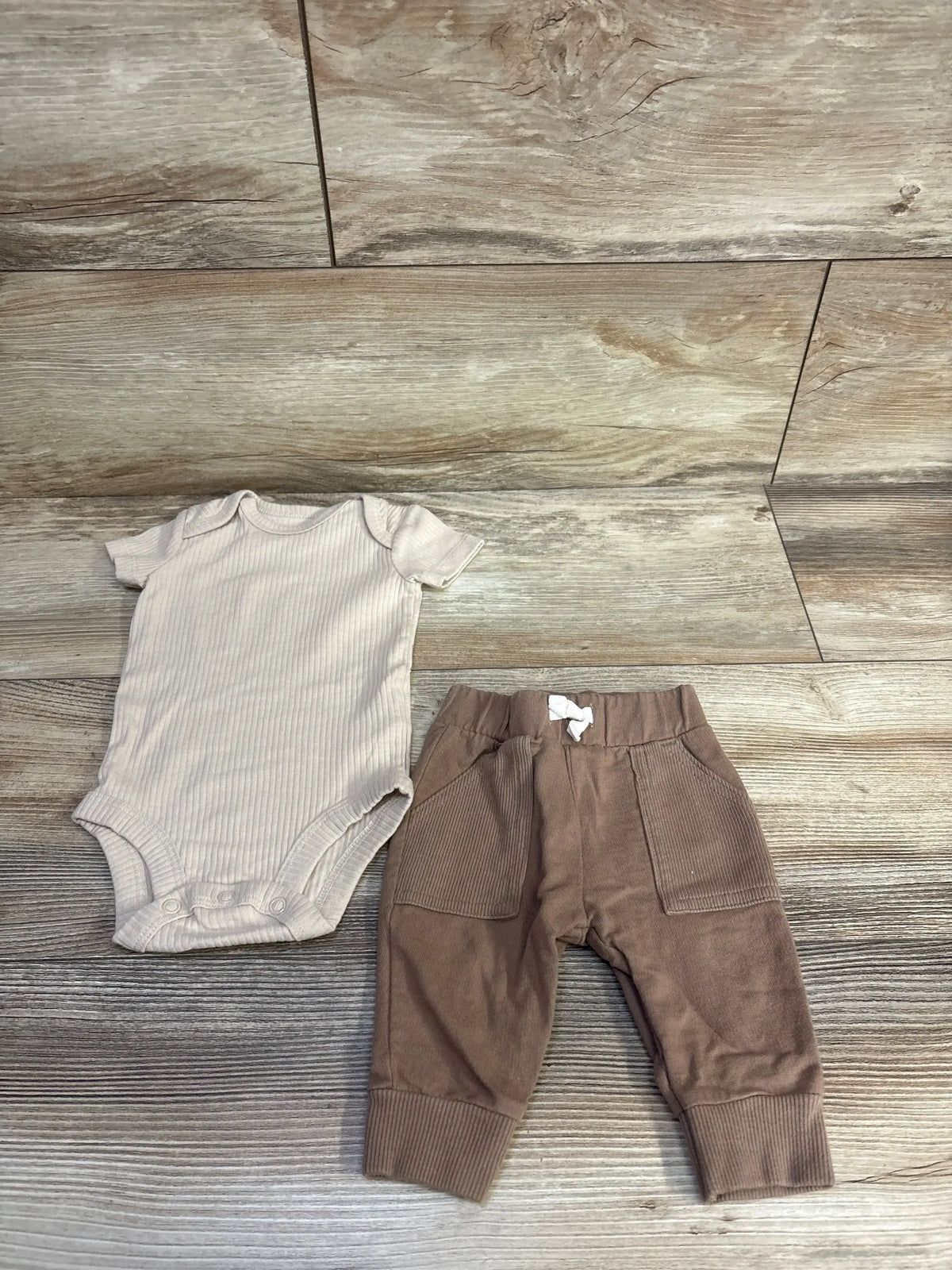 Flat lay of Carter's 2-piece set: beige ribbed short-sleeve bodysuit and brown pocketed cuffed pants on wood floor