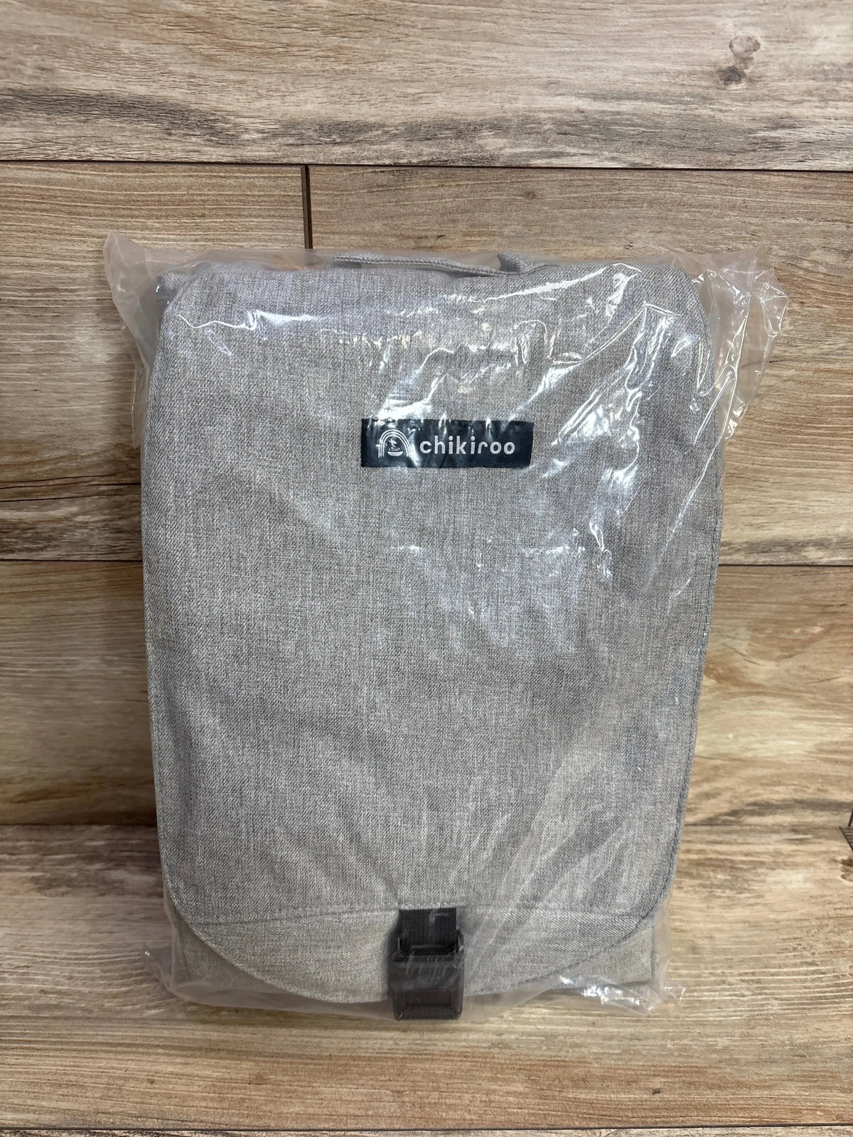 Front of Chikiroo wearable changing station, gray woven fabric with visible chikiroo logo and buckle, in sealed plastic on wood floor