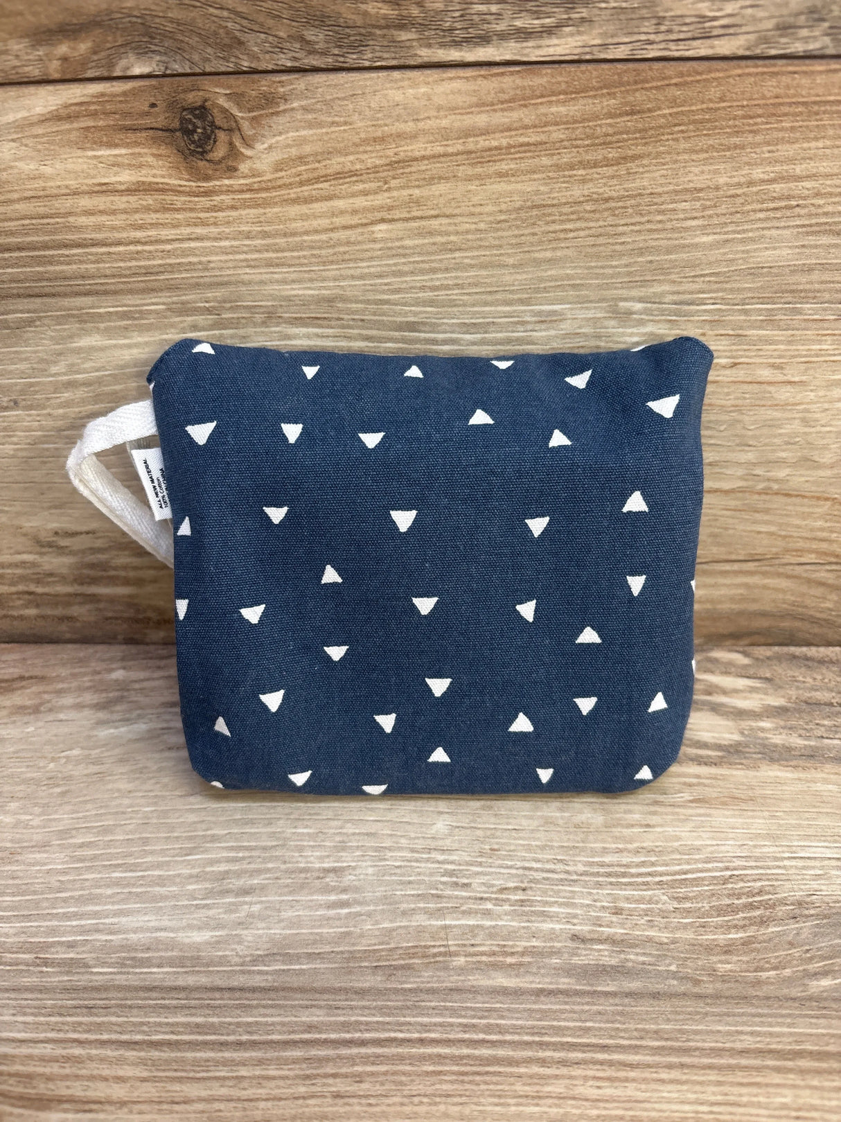 Front view of small navy fabric pouch with white triangle print and fabric loop handle on wooden background
