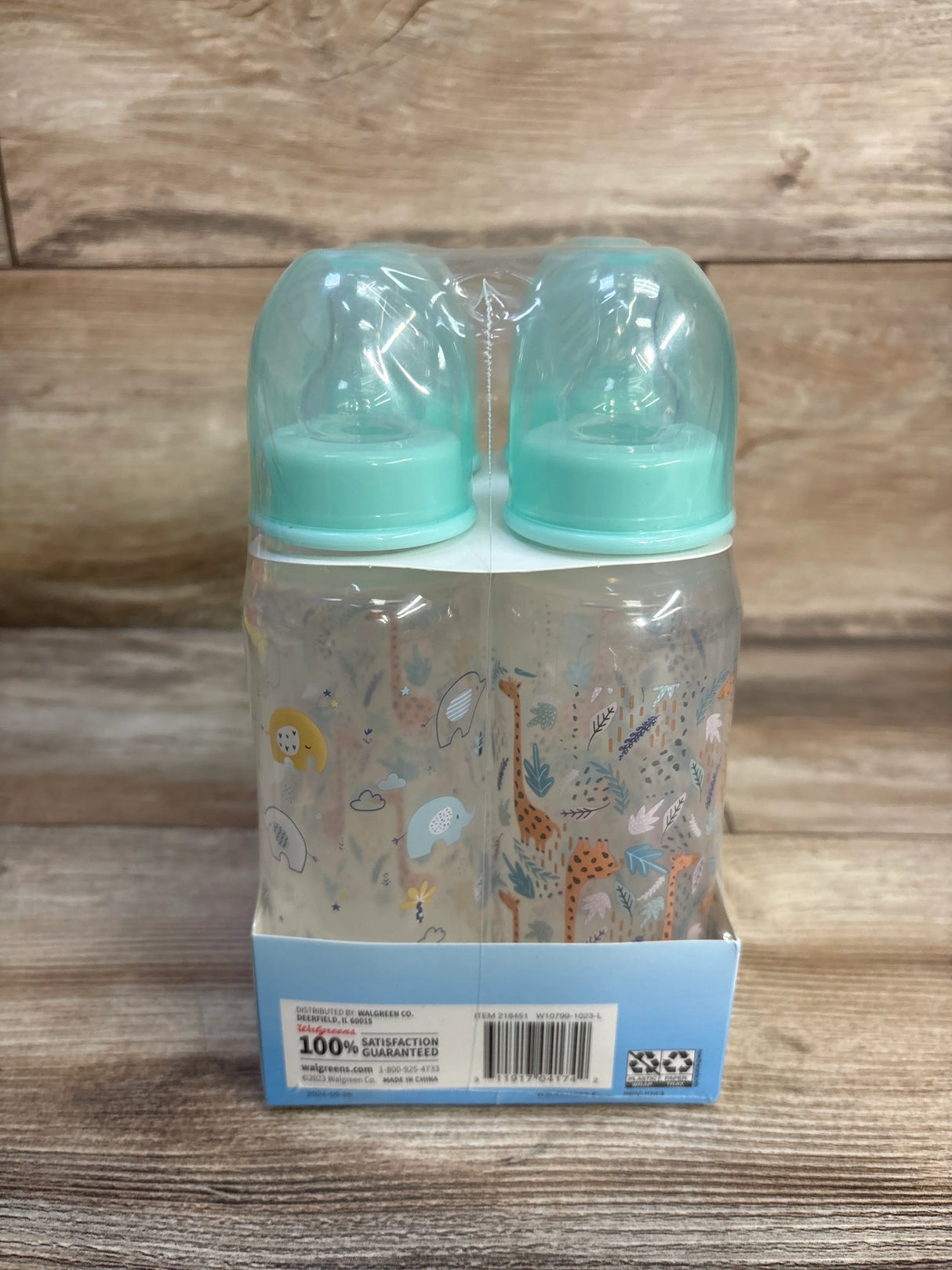Front view of a four-pack of Walgreens baby bottles showing mint caps and animal and leaf print with wood plank background