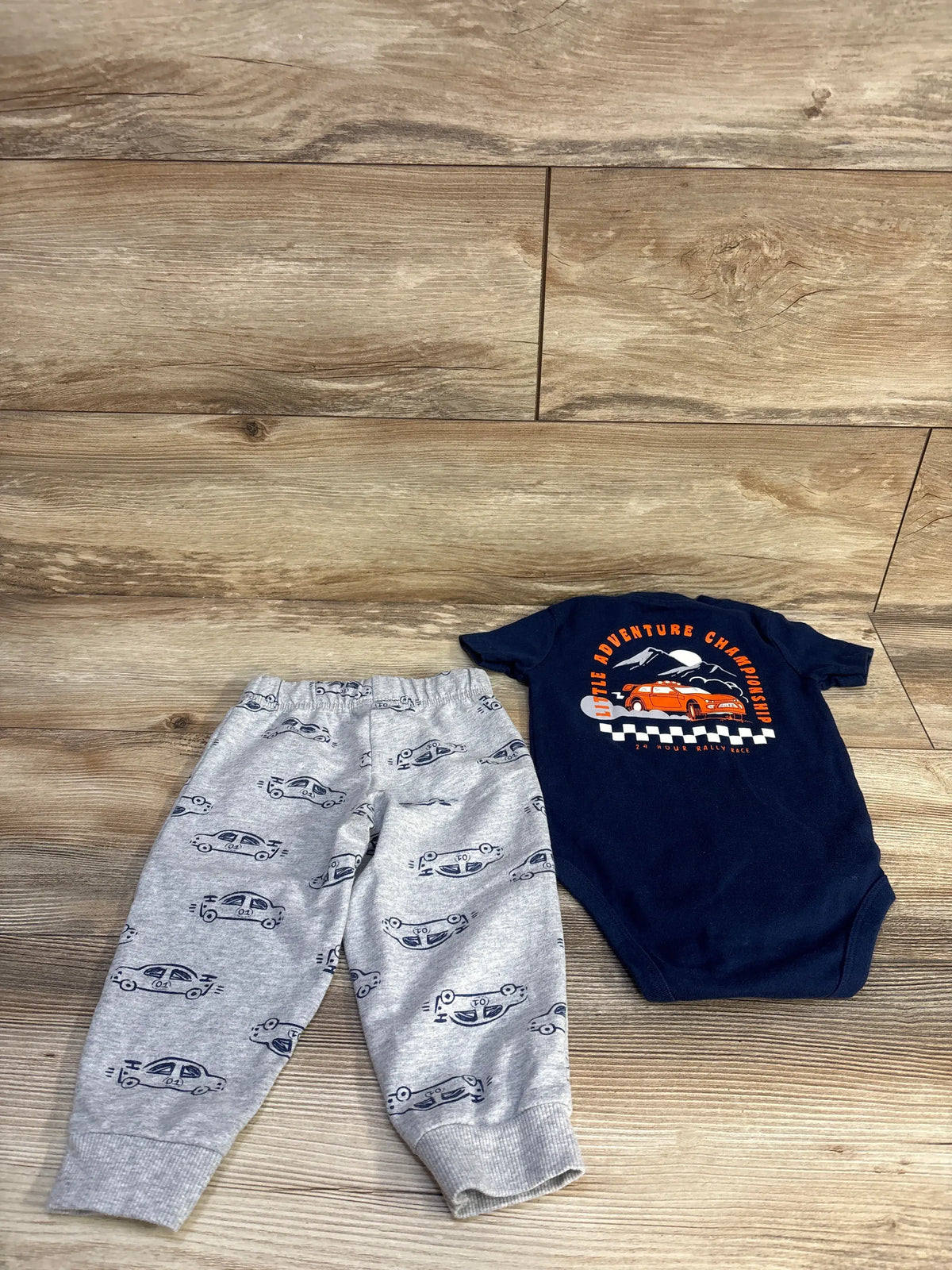 Top view of Carter’s two-piece bodysuit and shorts set showing a graphic navy bodysuit and patterned bottoms on wood floor