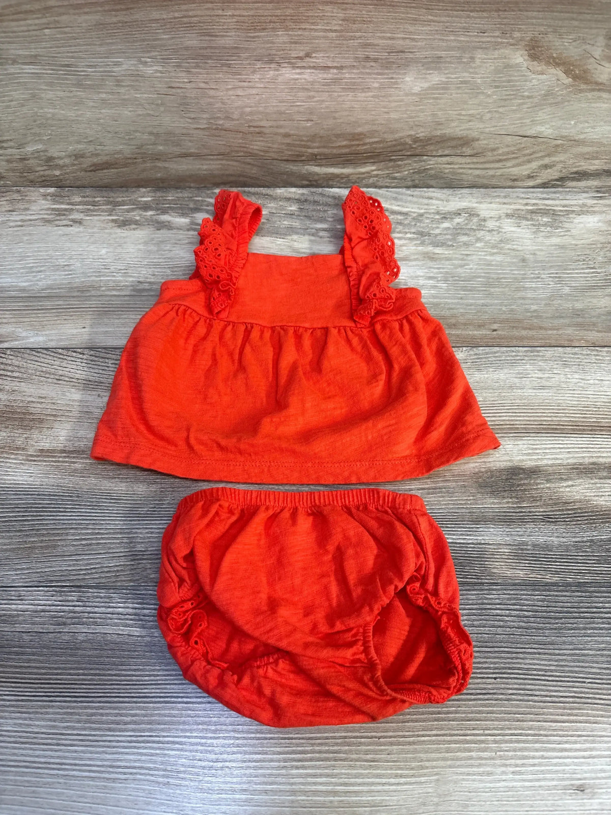 Flat lay of red Carter's peplum top and bloomers showing ruffled eyelet straps and elastic waist on wood background