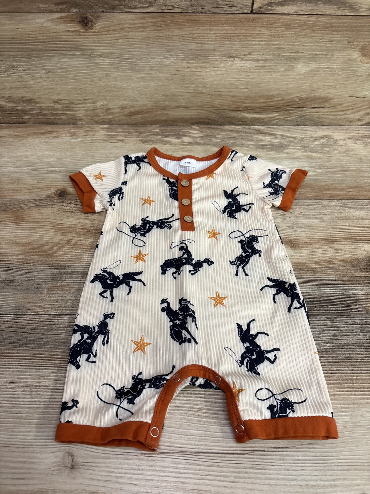 Front view of SAYOO Western Romper in cream, size 3-6M, showcasing cowboy and star print with brown trim on wood