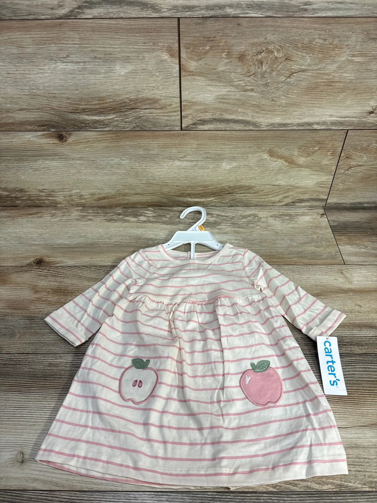 Carter's baby dress with pink stripes and apple patches, long sleeves, on wooden background