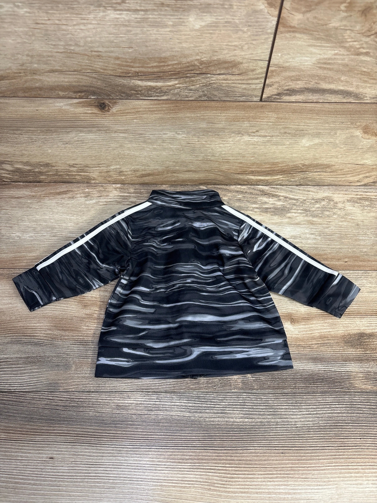 Black and gray toddler track jacket with white stripes on sleeves, laid on wood floor
