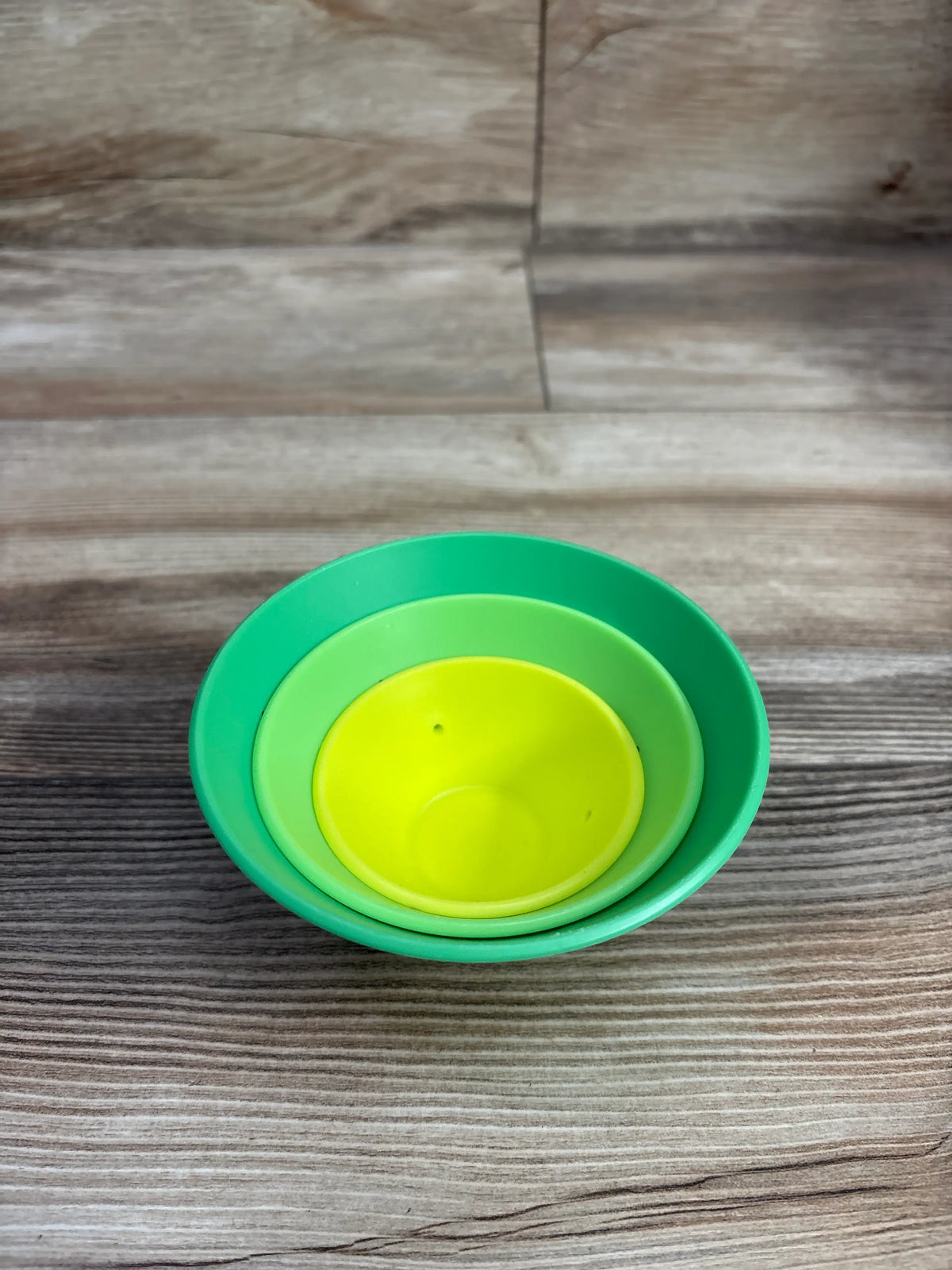 Top view of Lovevery Roll & Build Cone Set showcasing nested green and lime pieces on a wood-grain surface