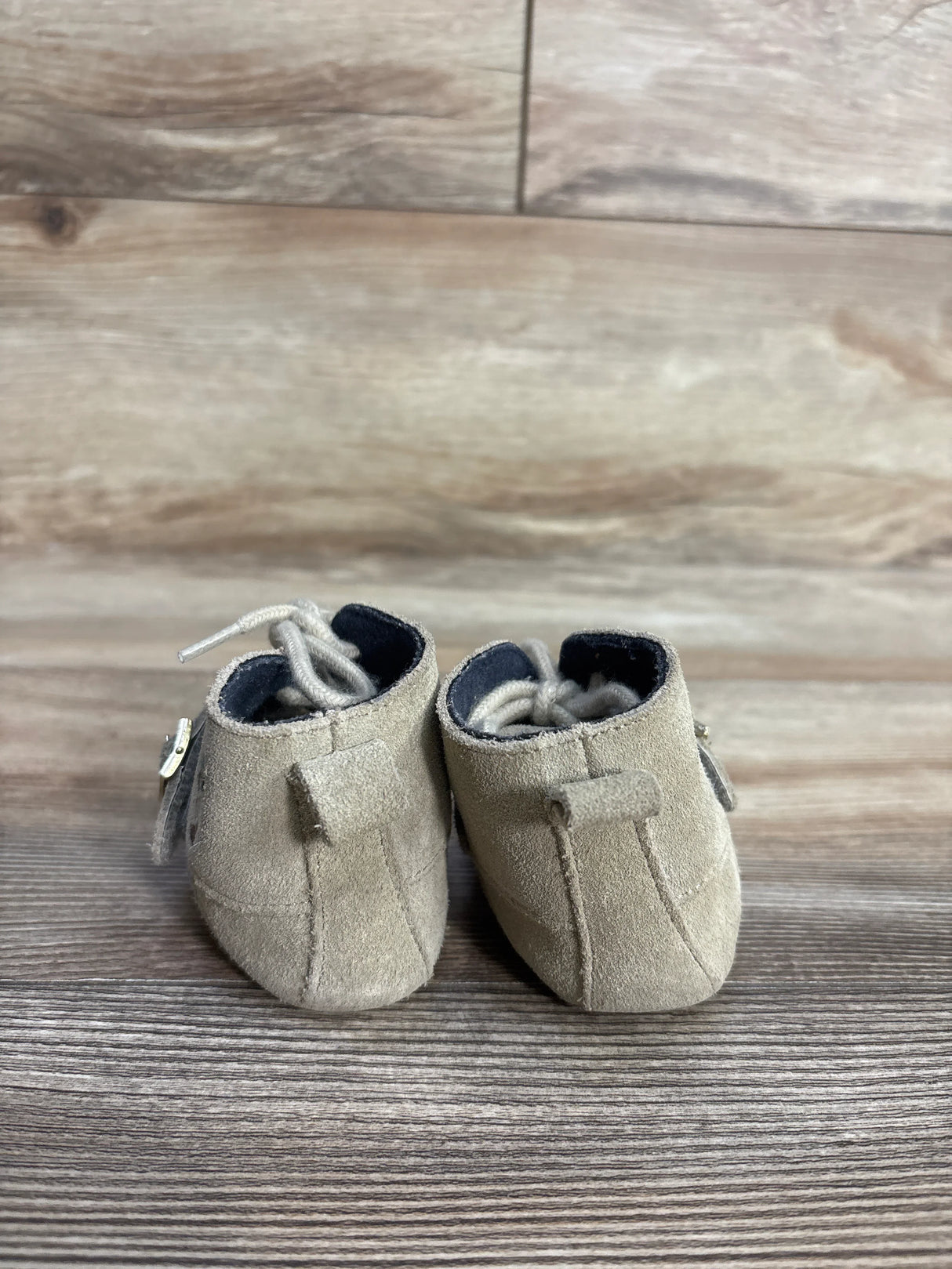 Back view of small beige suede baby shoes with laces on wood surface