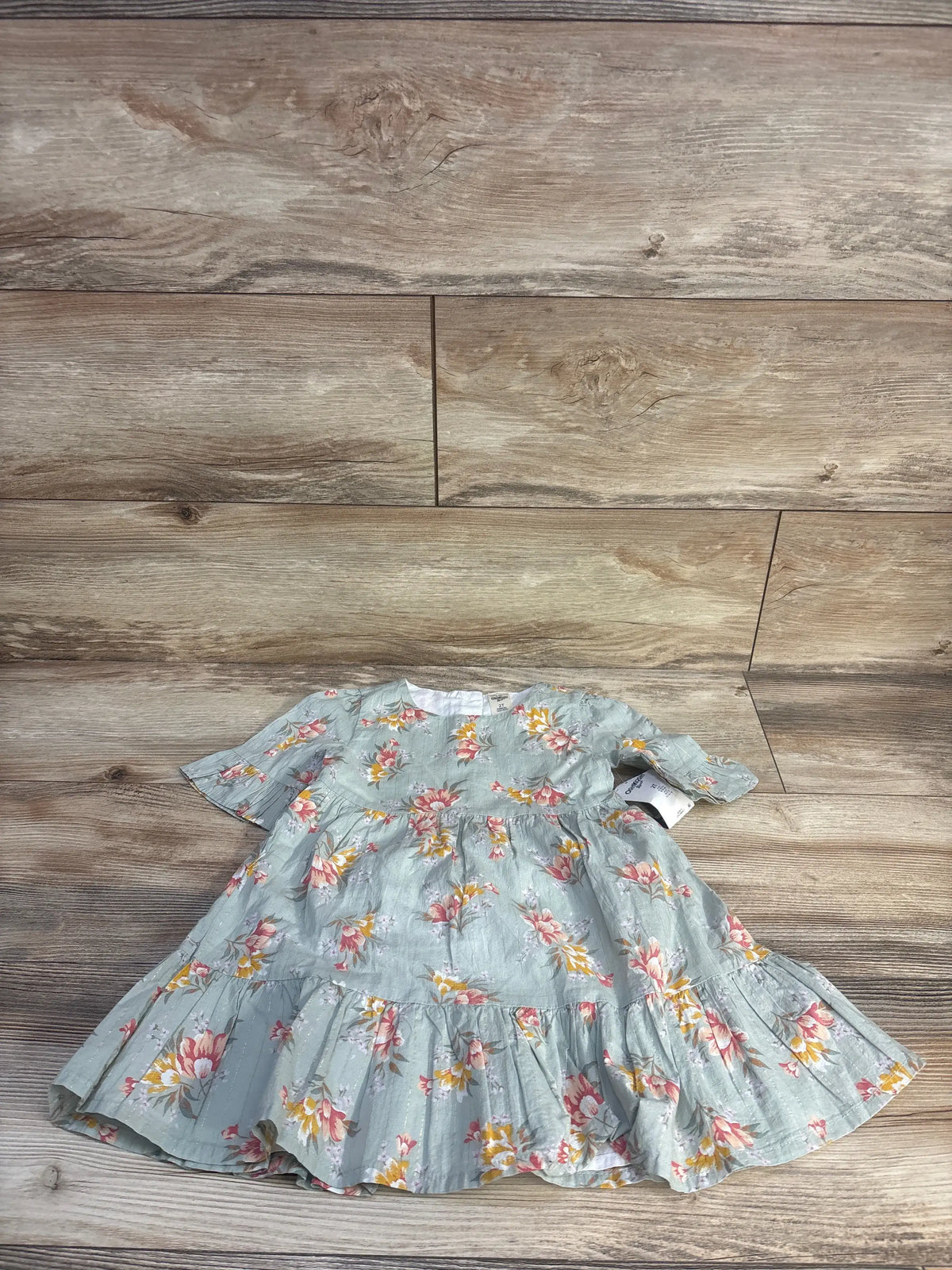 Front view of NEW Oshkosh floral dress in green, showcasing short sleeves and tiered skirt on a wood floor