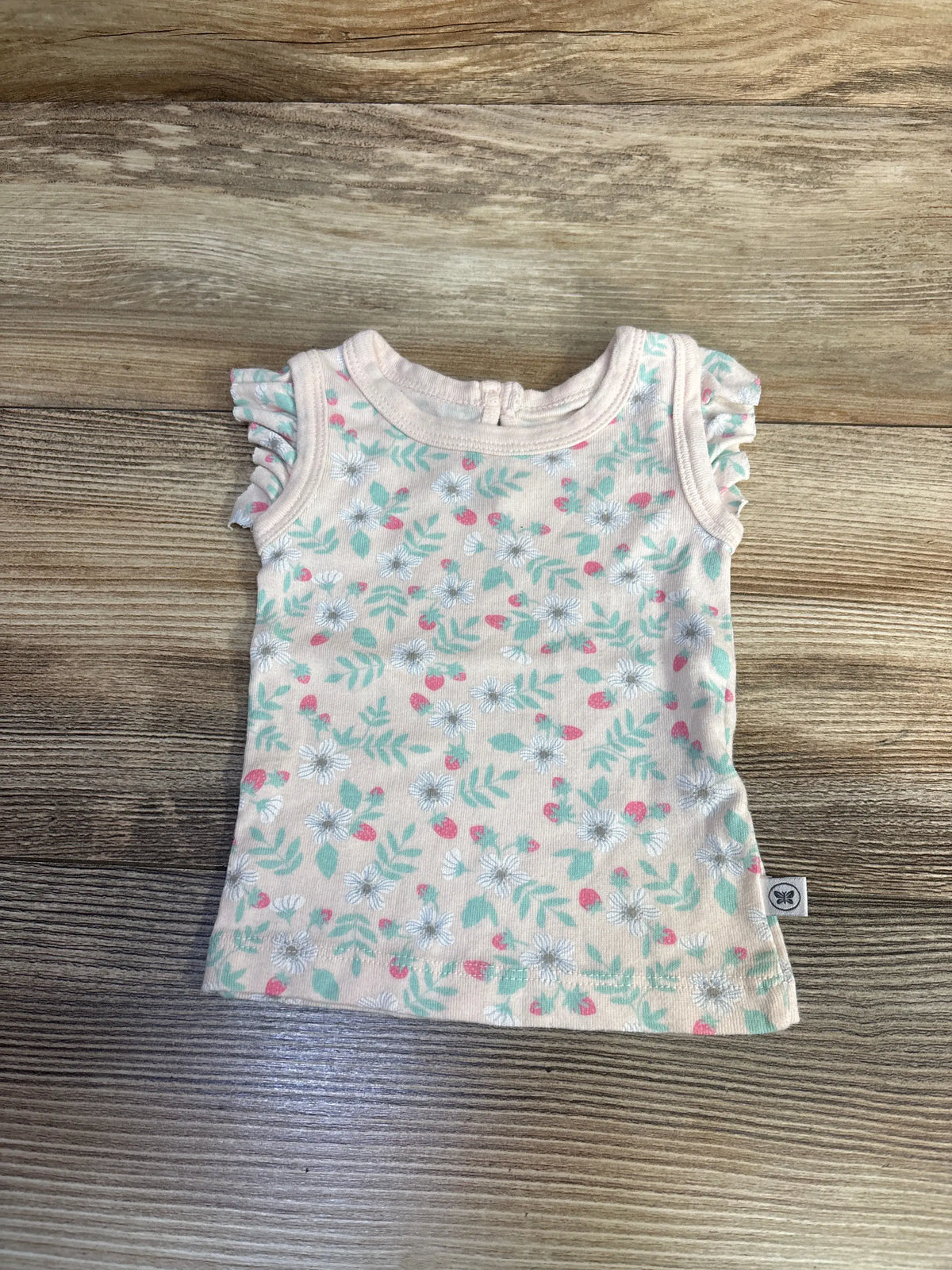Front view of the pink Honest Baby floral tank top showcasing ruffled shoulders on a wood-grain background