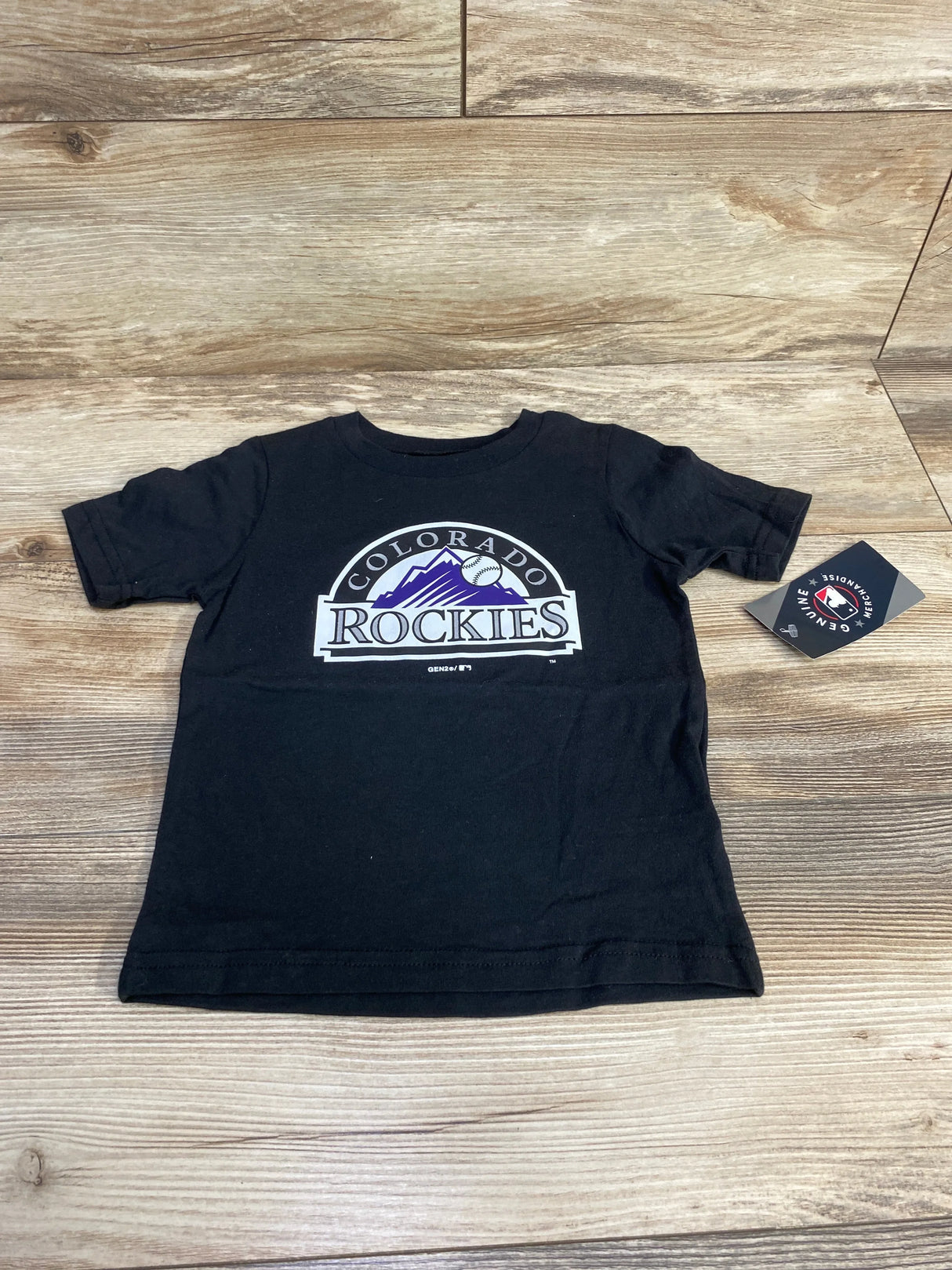 Flat lay of black Colorado Rockies toddler t-shirt (3T) showing front team logo and attached tag on wood background
