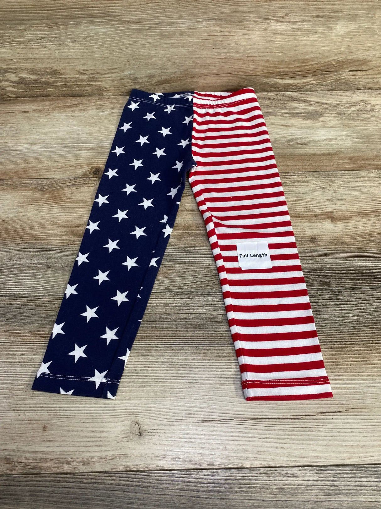 Flat lay of Old Navy toddler leggings (size 3T) showcasing navy leg with white stars and red-and-white striped leg with light wood background