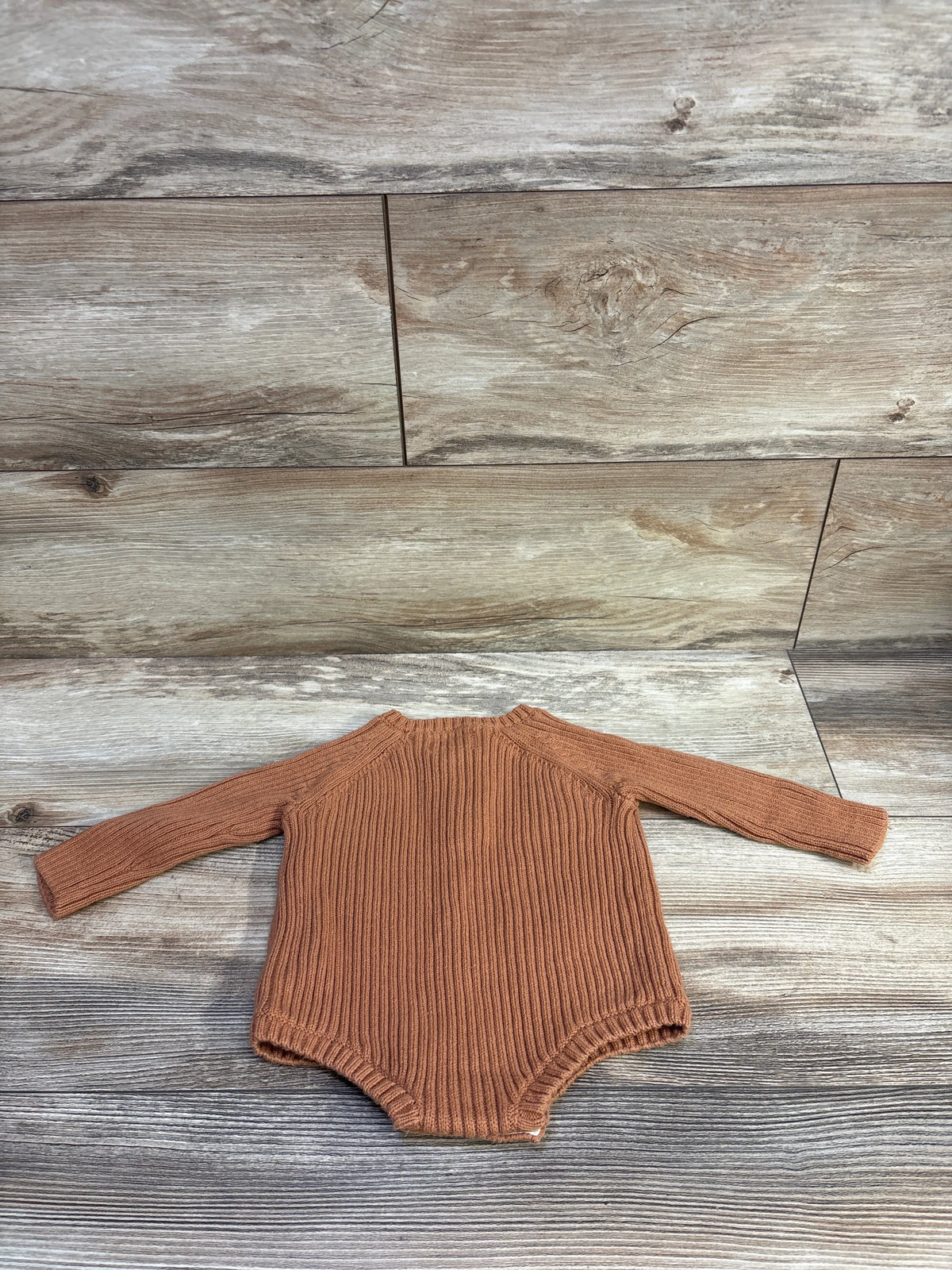 Top view of Little Planet knit henley bodysuit showcasing brown ribbed knit and long sleeves on a wood background
