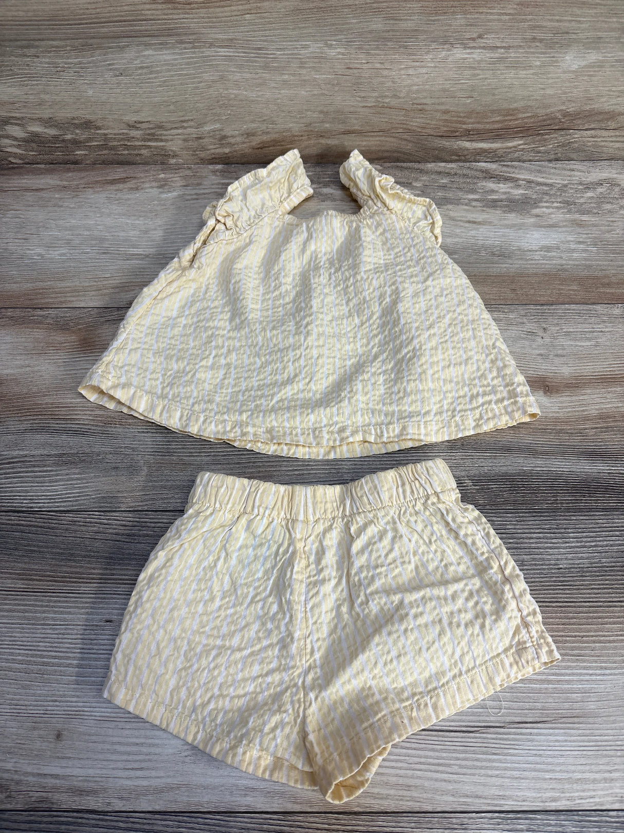 Yellow and white striped baby outfit with ruffled top and shorts, laid on wood floor