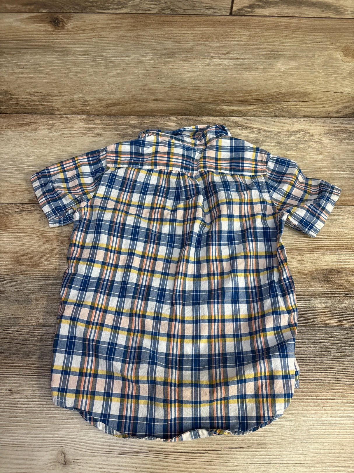 Blue, white, and yellow plaid short-sleeve shirt laid flat on a wooden surface