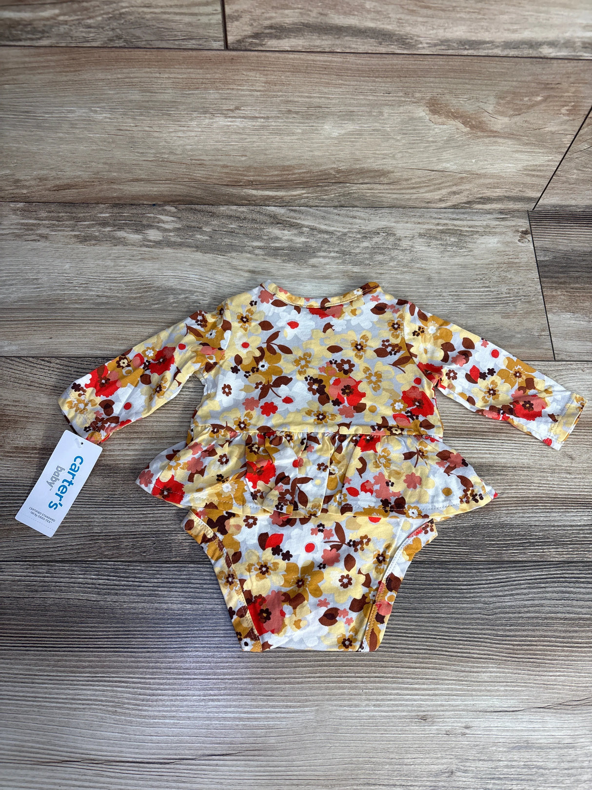 Carter's baby floral long-sleeve onesie with yellow, red, and brown flowers on wood floor