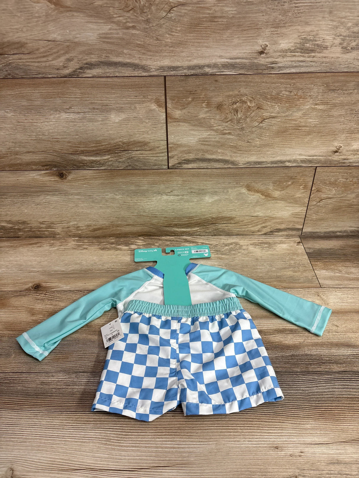 Flat lay of Disney baby rash guard set with light-blue long-sleeve top and blue-white checkered swim shorts on wood