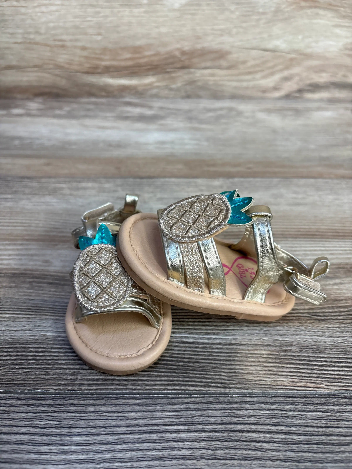 Front view of NEW 143 Girls Pineapple Sandals sz 1c with metallic pineapple appliques and ankle straps on a wood-grain surface