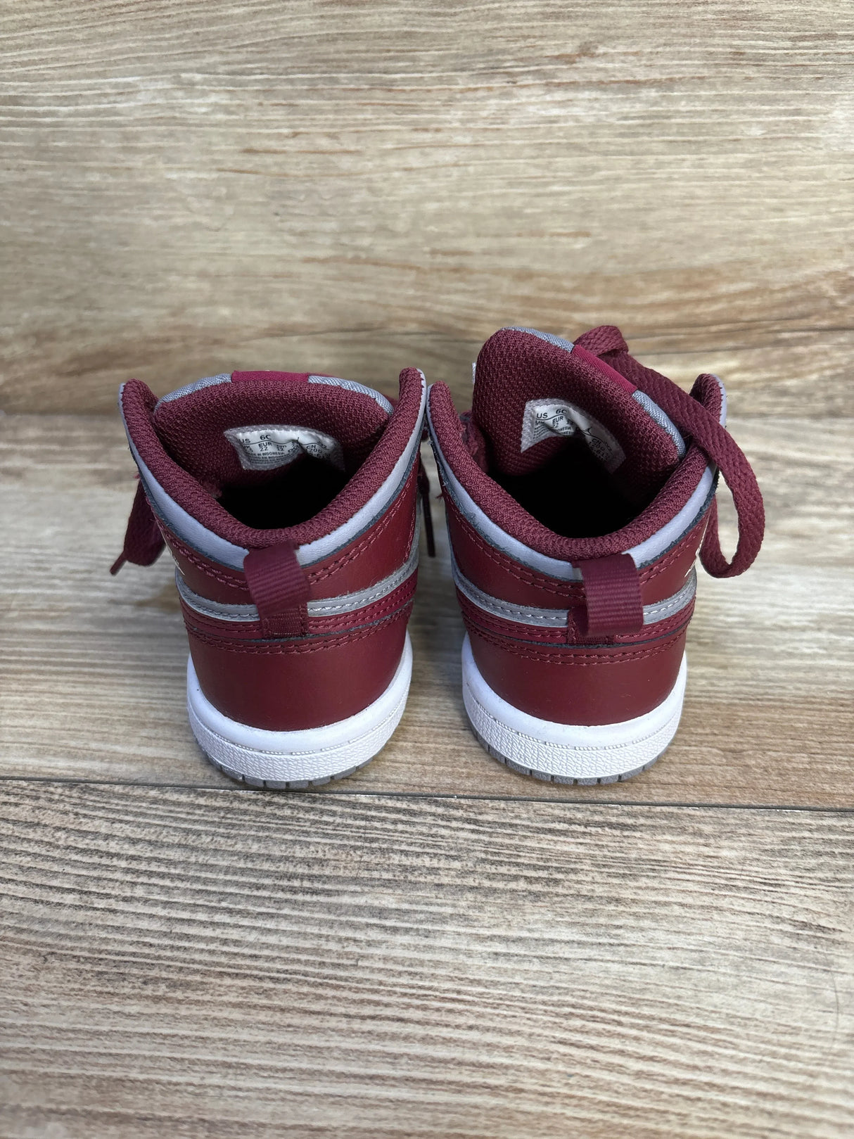 Back view of Air Jordan 1 Mid TD Cherrywood Red sneakers sz 6c showcasing maroon and grey heel panels on wood plank floor