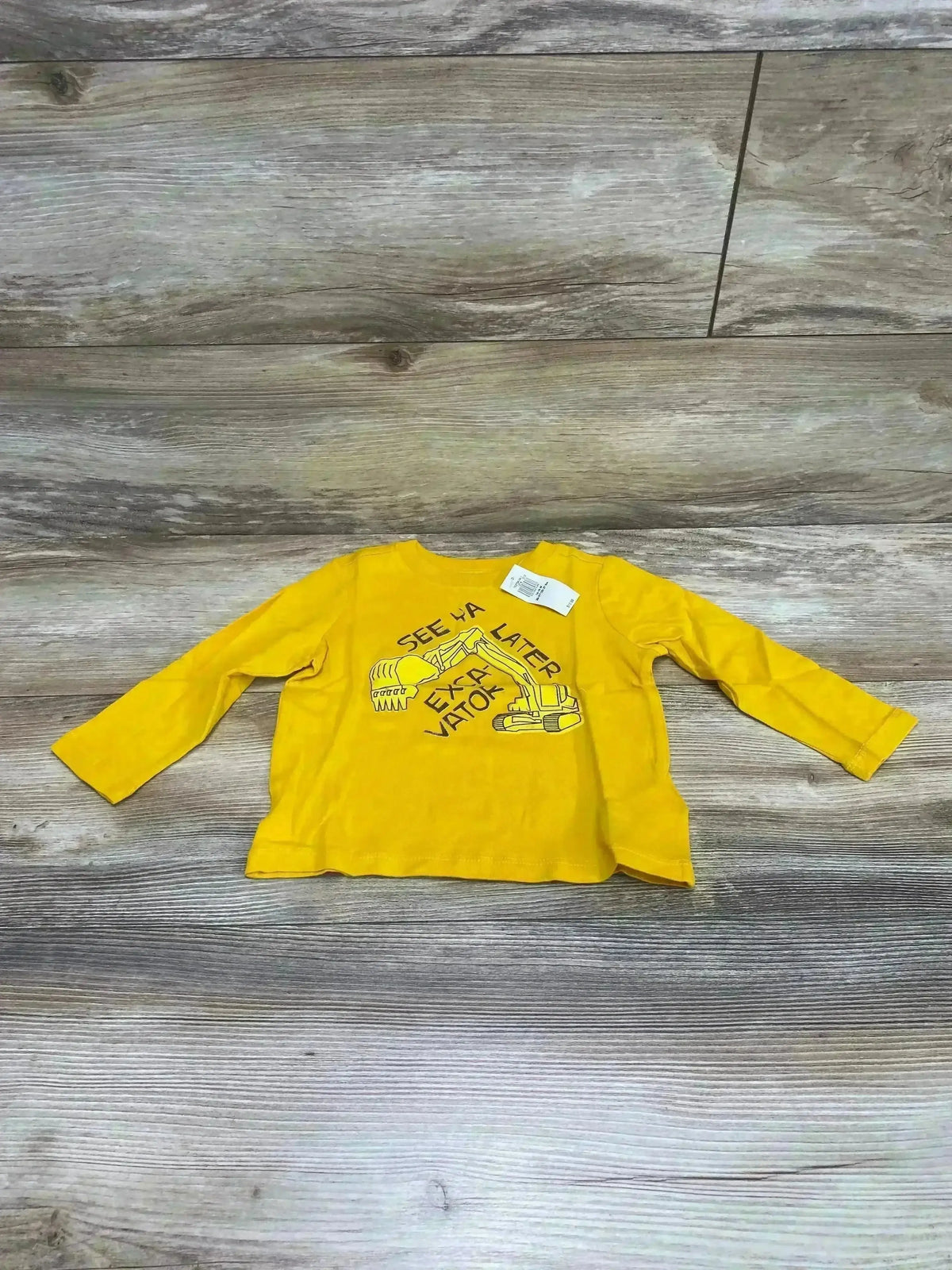 Flat lay of yellow Old Navy toddler long-sleeve shirt (12-18 months) showing excavator graphic and tag on wood floor background