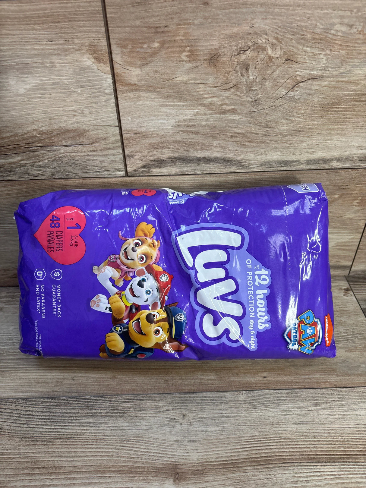Top view of Luvs Paw Patrol diaper pack, size 1 (48 ct), purple packaging with Paw Patrol characters on wood floor