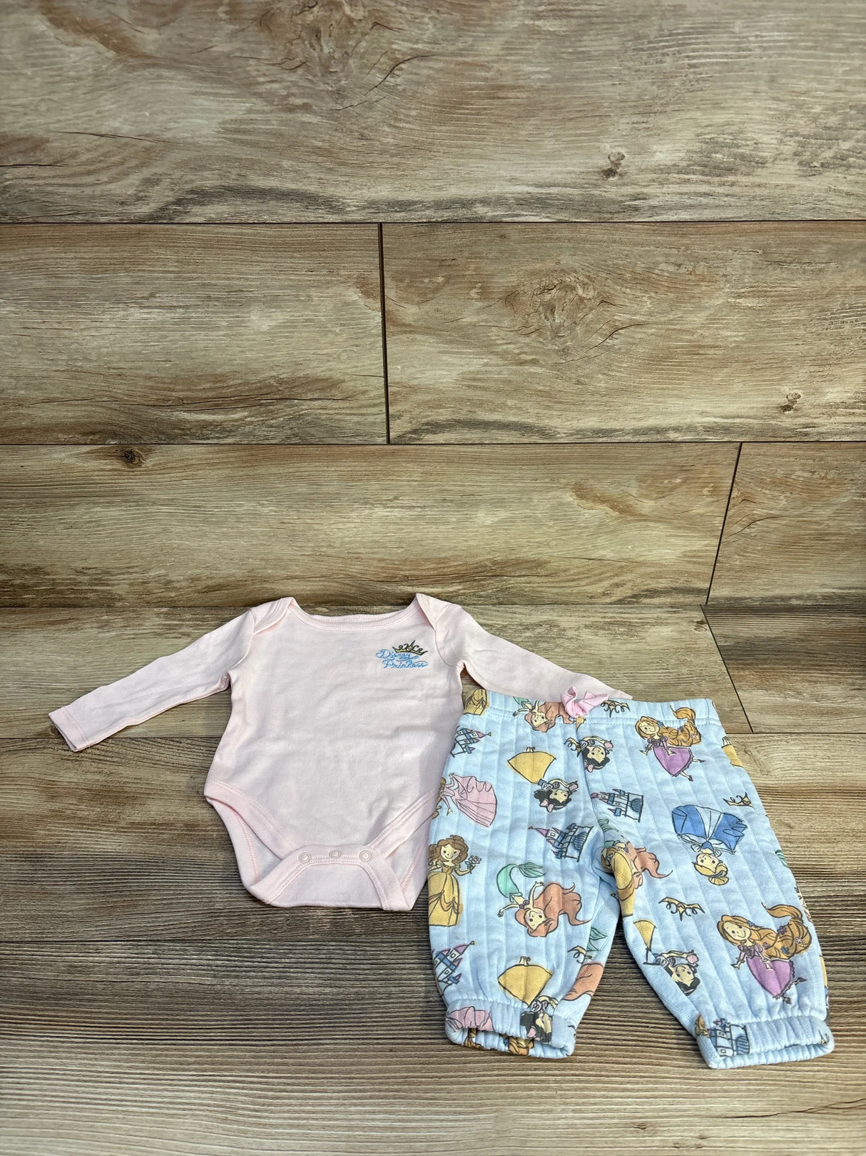 Pink Disney Princess baby onesie with blue princess print pants, kids clothing set on wood floor